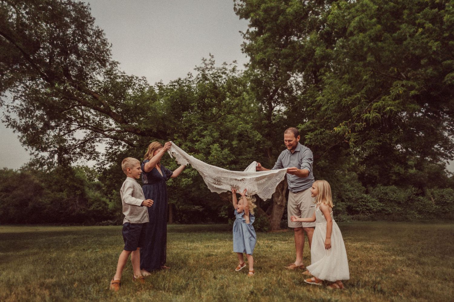 Family playing together with white fabric in a grassy outdoor setting during golden hour.