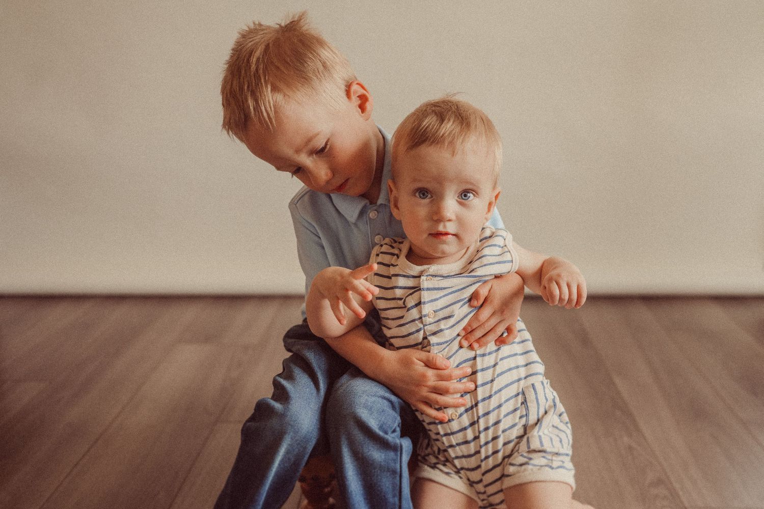 Two playful kids sharing a tender moment together on hardwood flooring.