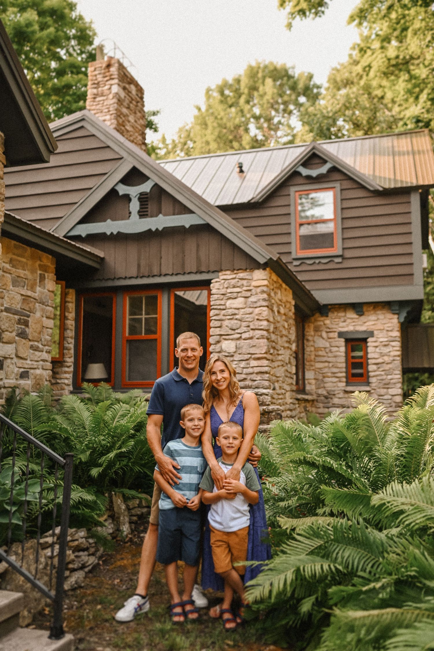 Family portrait in front of a beautiful stone and wood cottage with ferns landscaping.