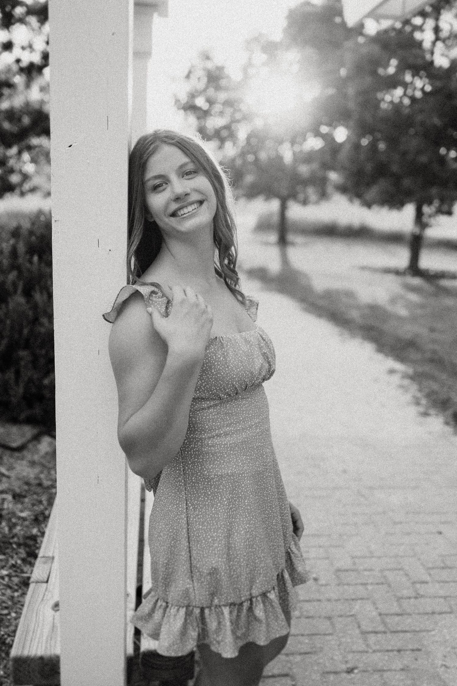 Black and white portrait against white column with sunburst through trees.