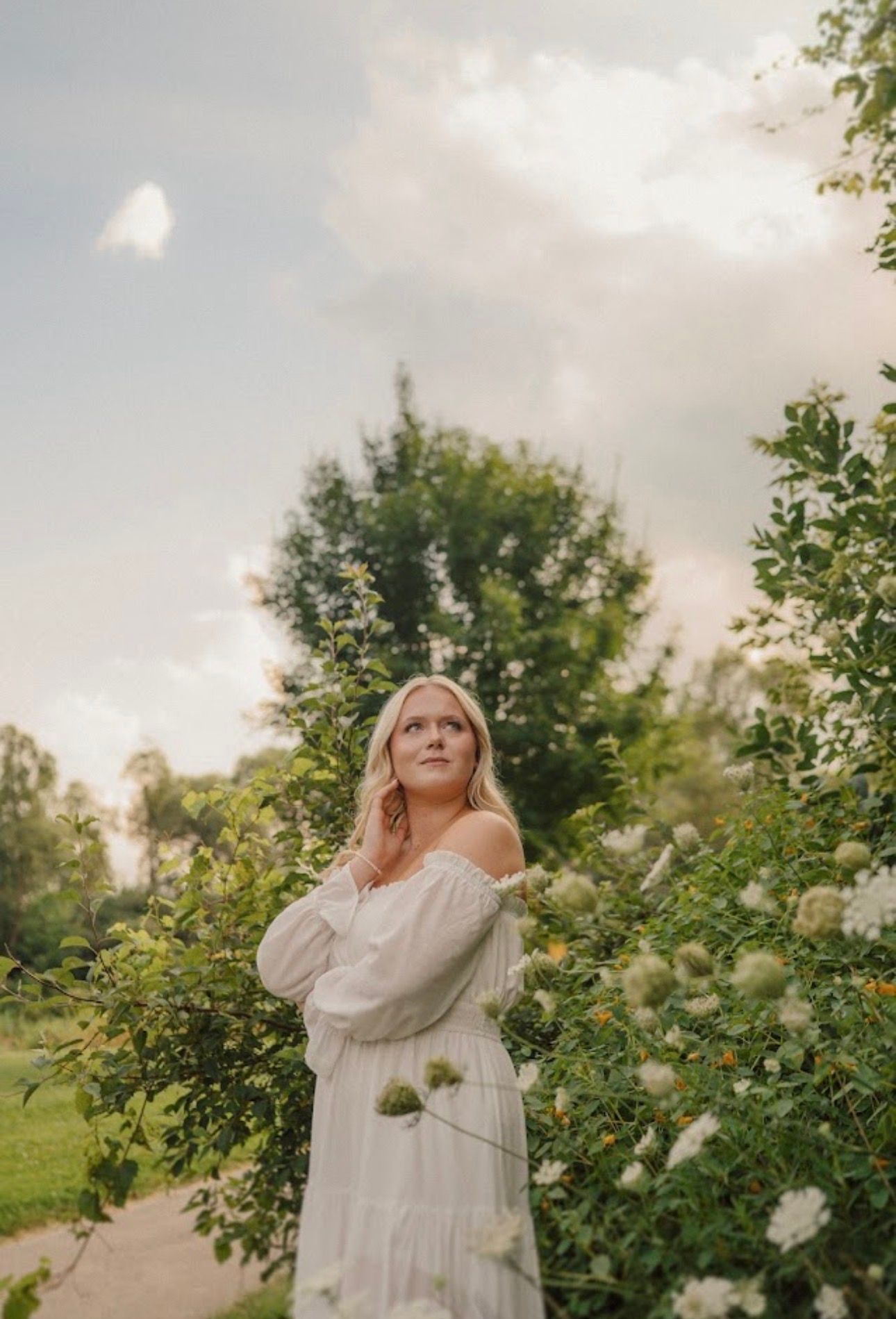 A dreamy photoshoot in a garden with white flowers and sunlit trees creating an ethereal atmosphere.