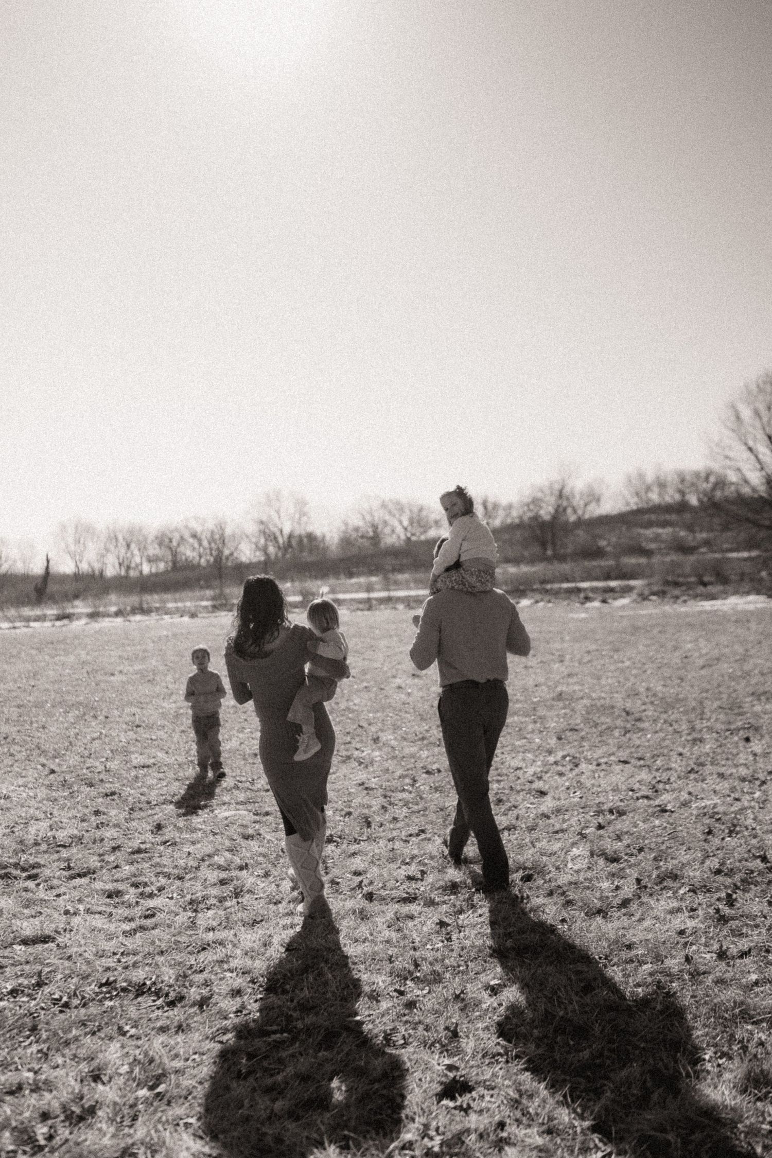 Silhouettes of people walking across an empty field casting dramatic shadows in the late afternoon light.