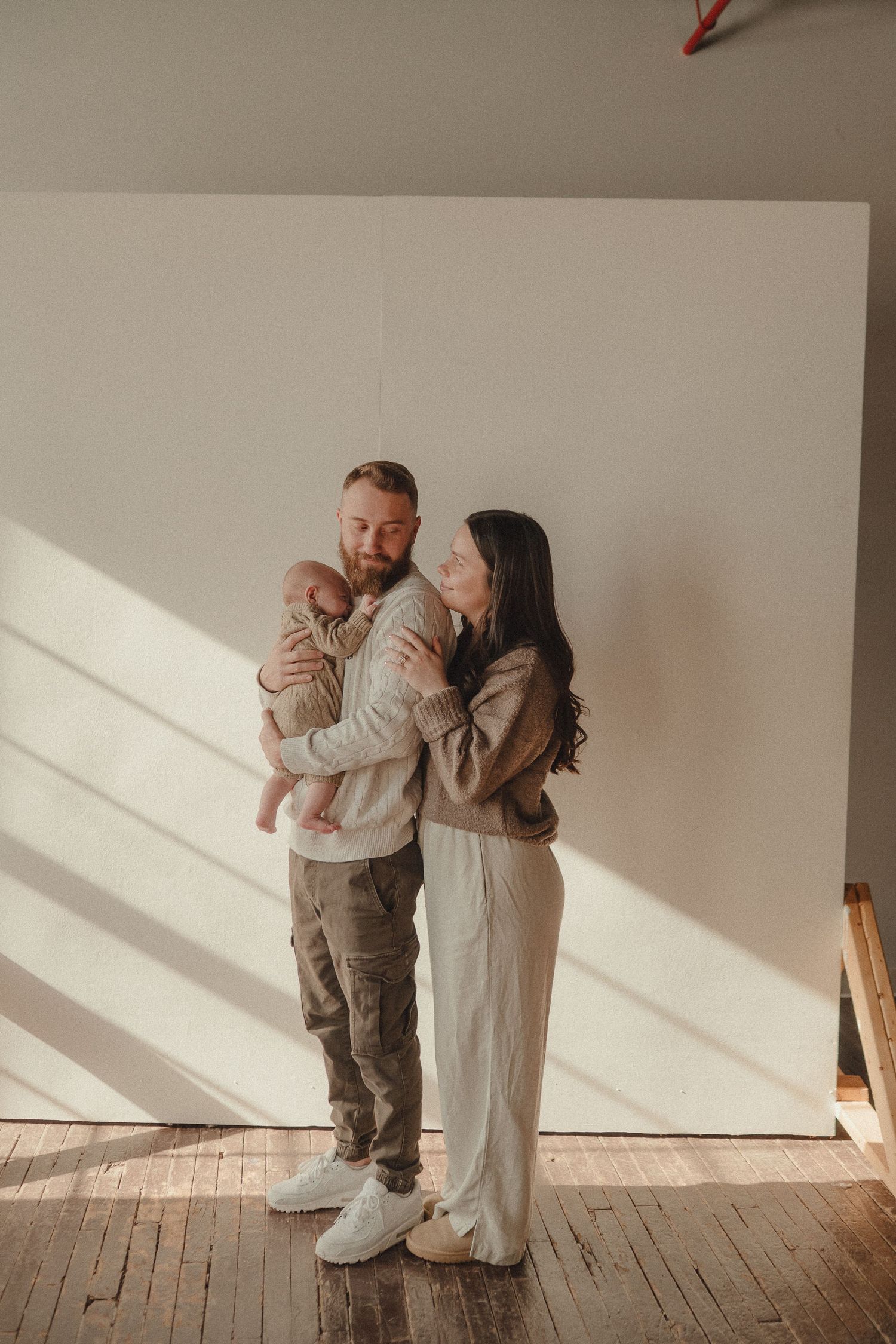 Natural light photography session on wooden floors with diagonal shadows.