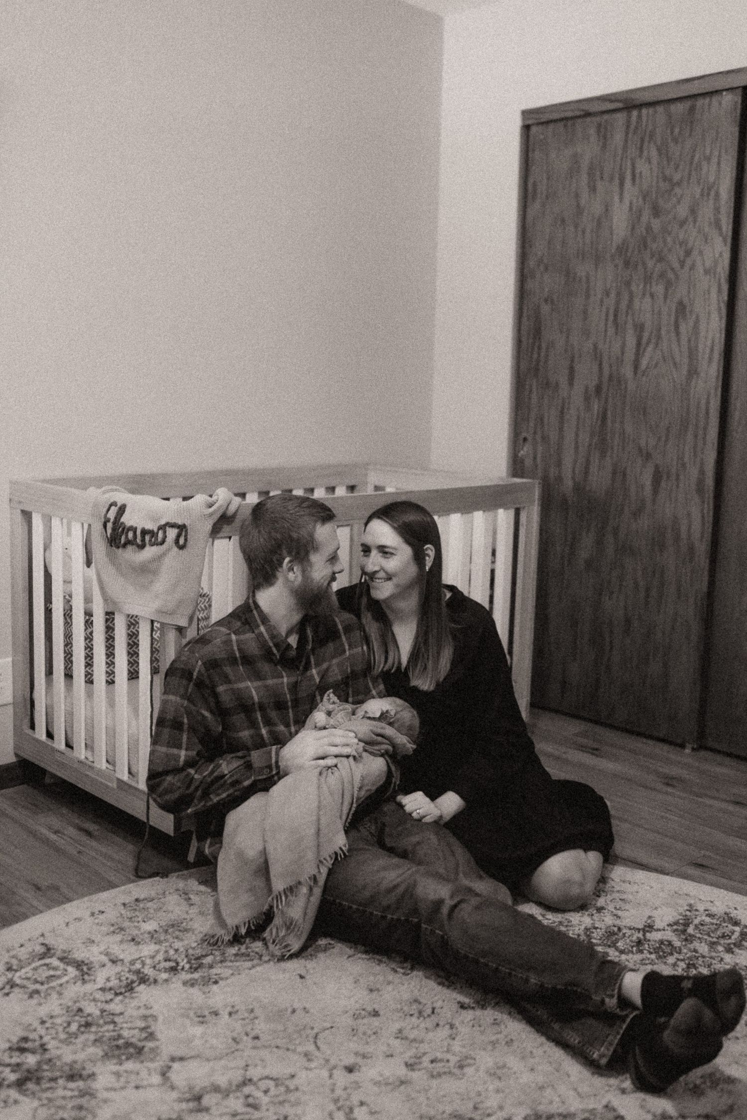 A heartwarming scene of family bonding while lying on a patterned rug near a white crib.