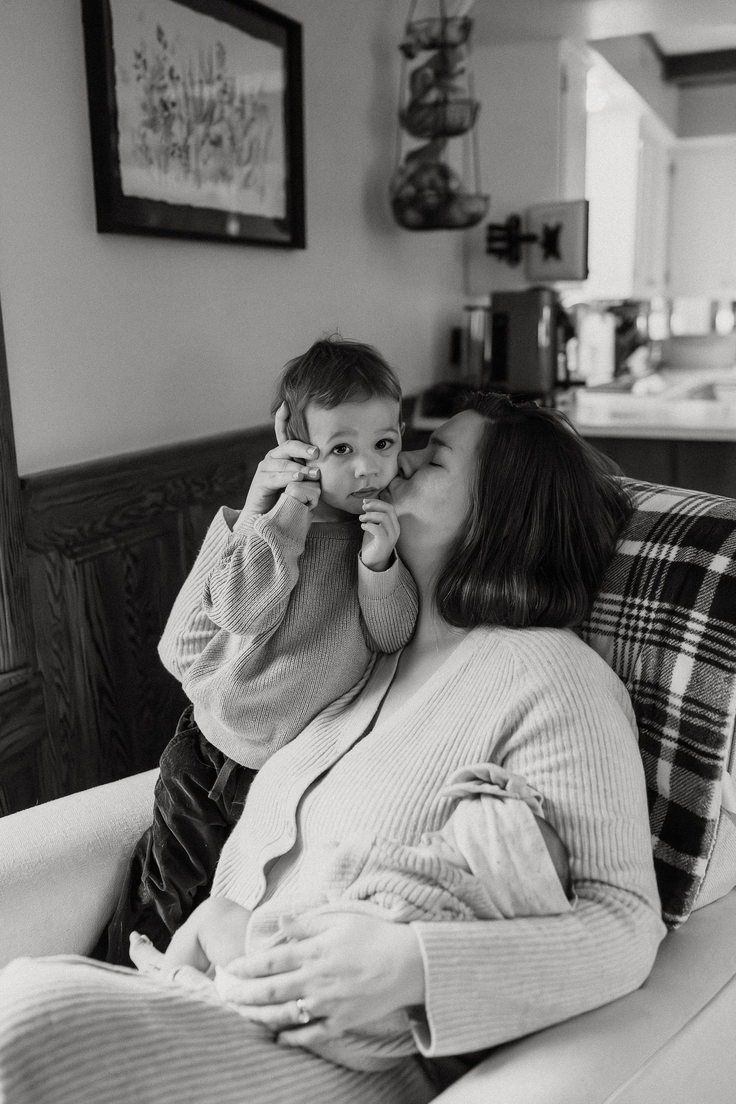 Intimate family moment captured in black and white on a plaid couch.
