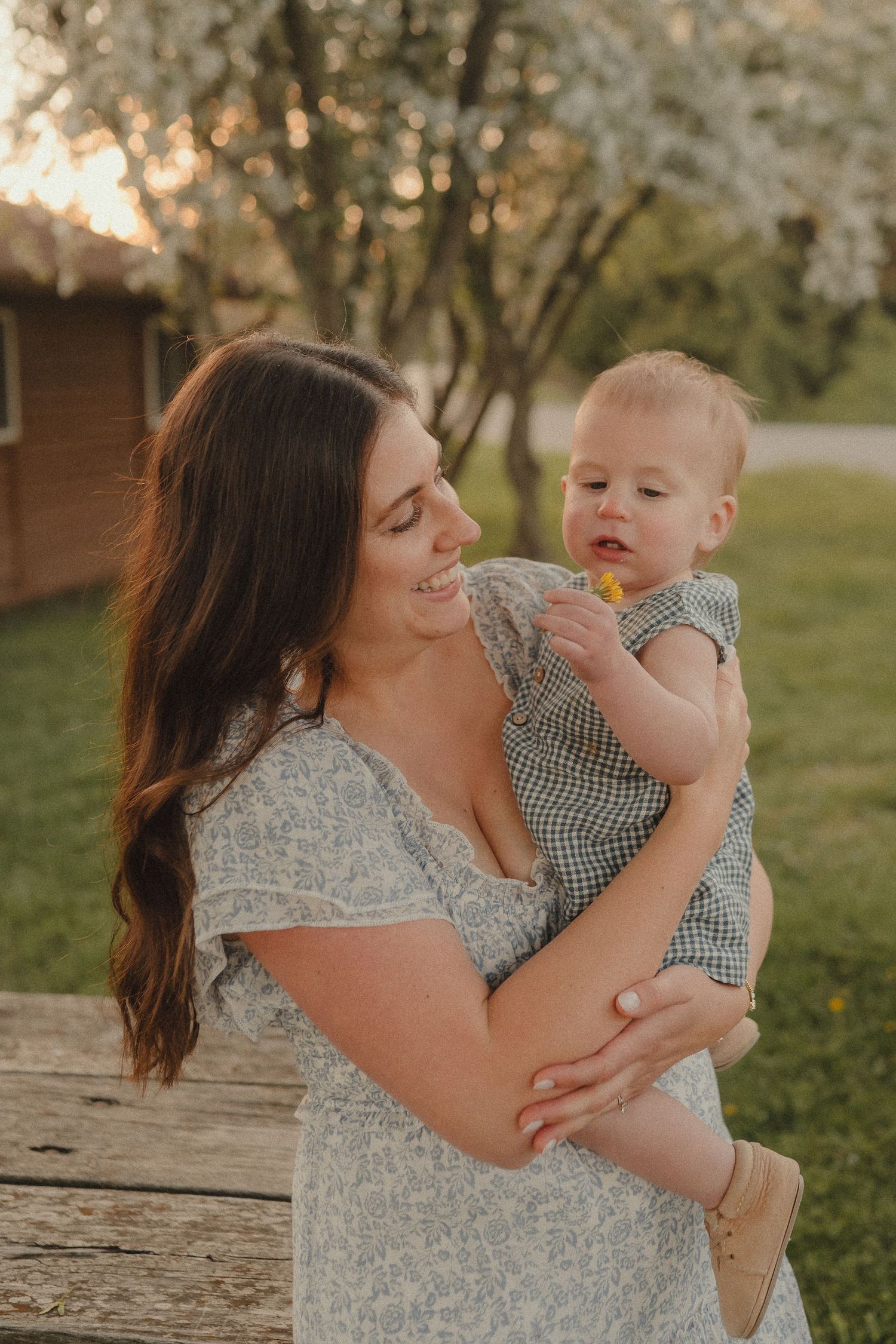 Loving mother in floral dress holding and gazing at her baby boy in a sunny garden.