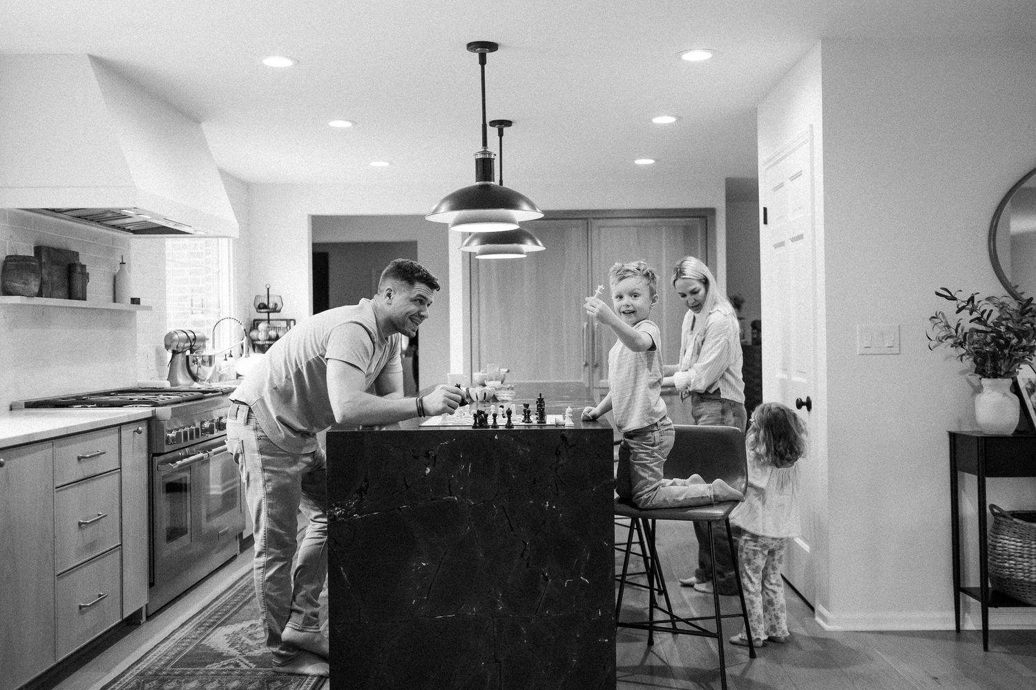 A family gathers around a kitchen island playing chess in a modern black and white home interior.