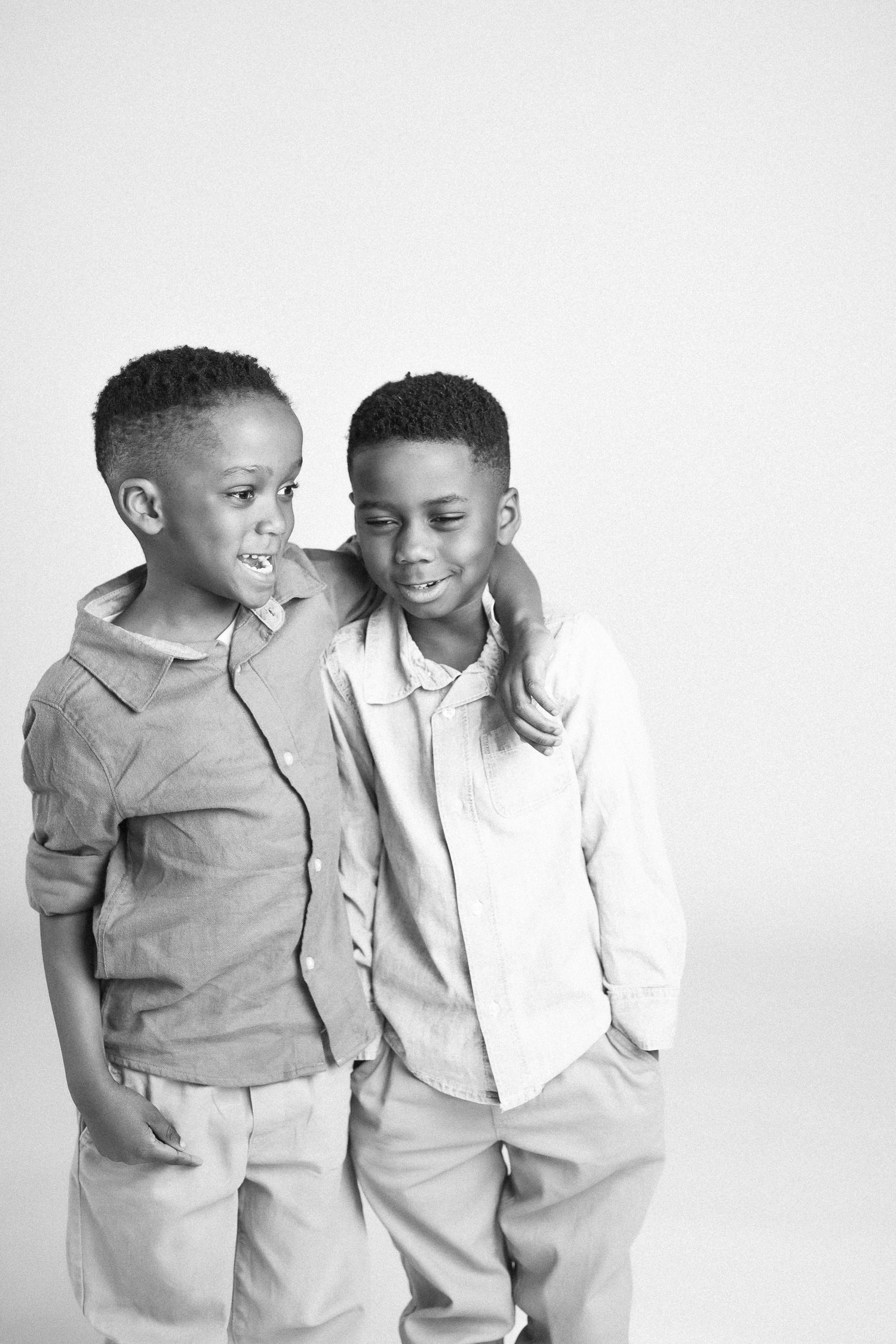 Two young children in casual outfits share a playful moment together in black and white photography.