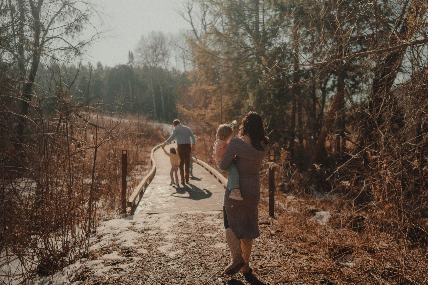 People walking along a nature trail surrounded by autumn foliage and trees at sunset.
