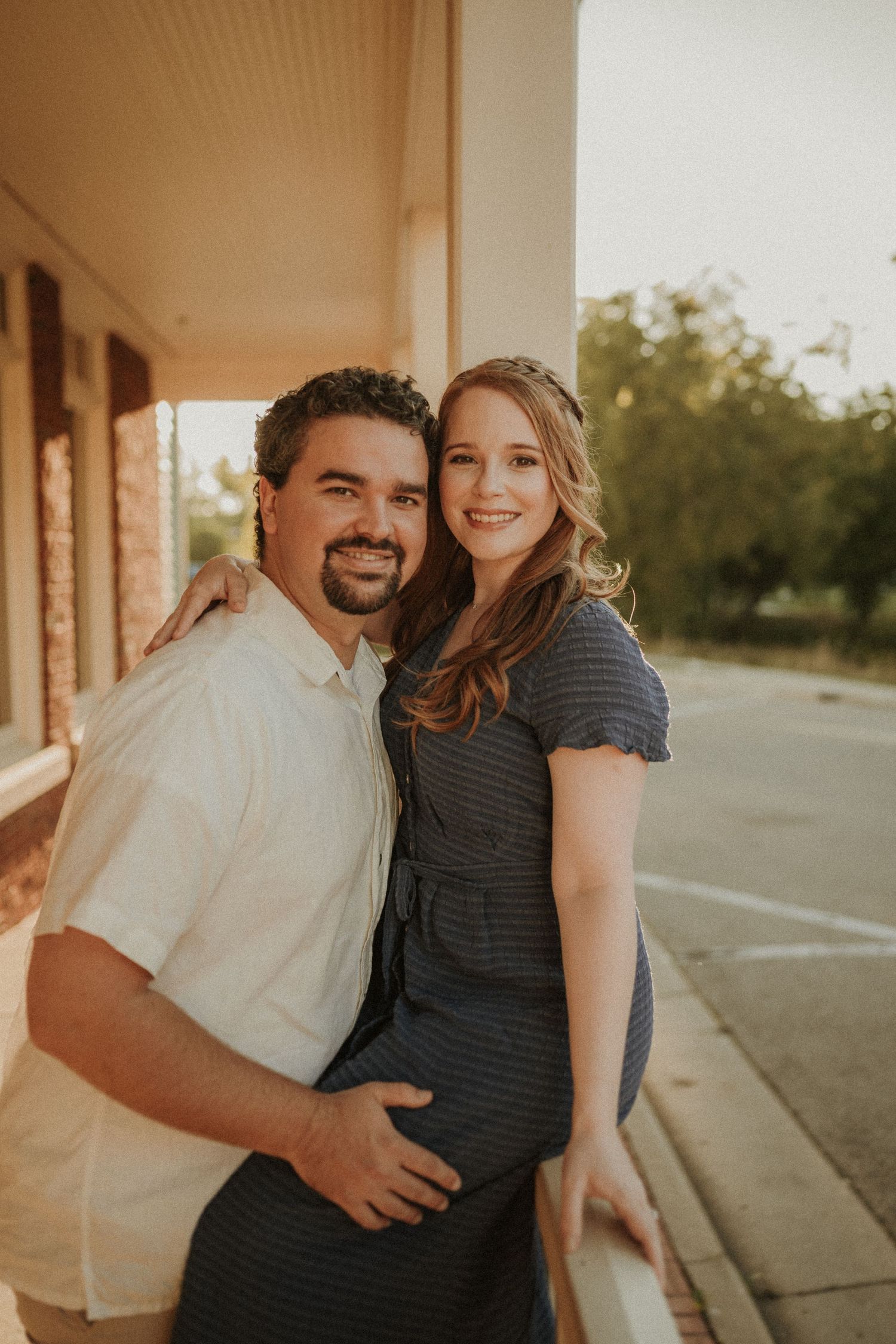 Happy couple posing together on a covered porch during golden hour.