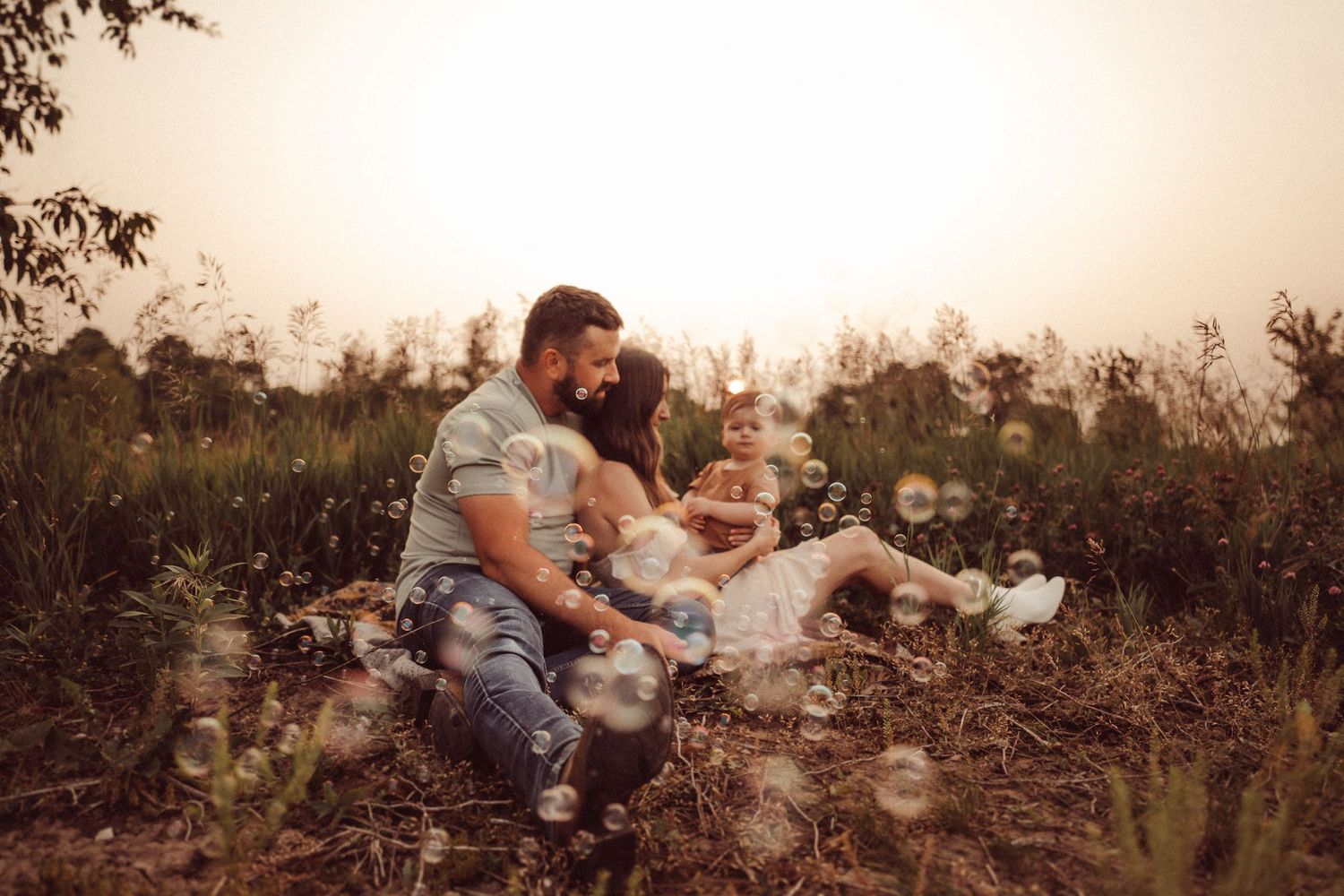 Warm-toned family photo session in a wild grass field at dusk.