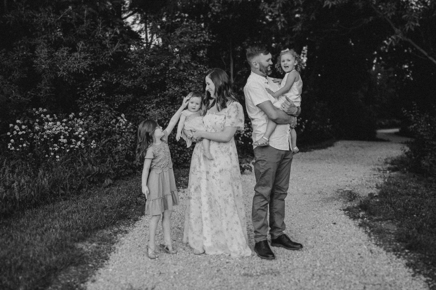 A black and white family portrait on a tree-lined path showing closeness and connection.