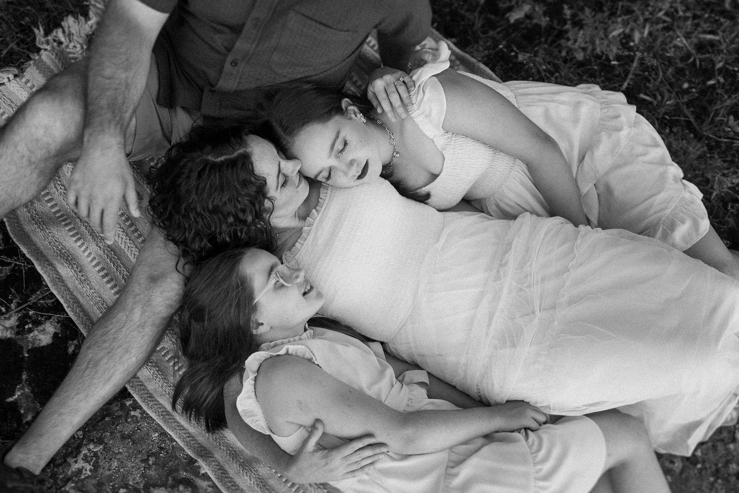 A tender black and white portrait of family members lying together on grass outdoors.