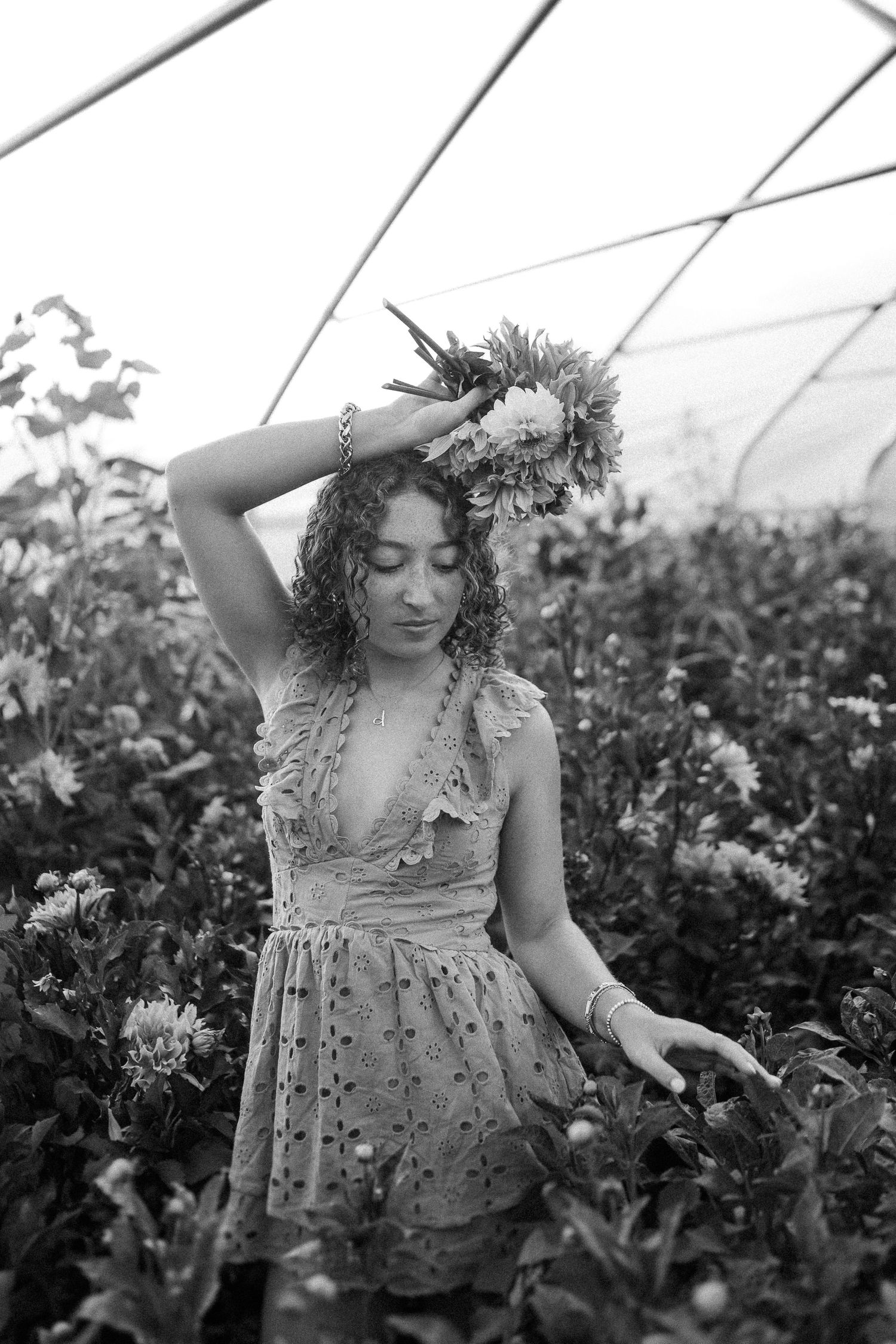 A whimsical summer portrait in a greenhouse with a floral dress amidst blooming plants in black and white.