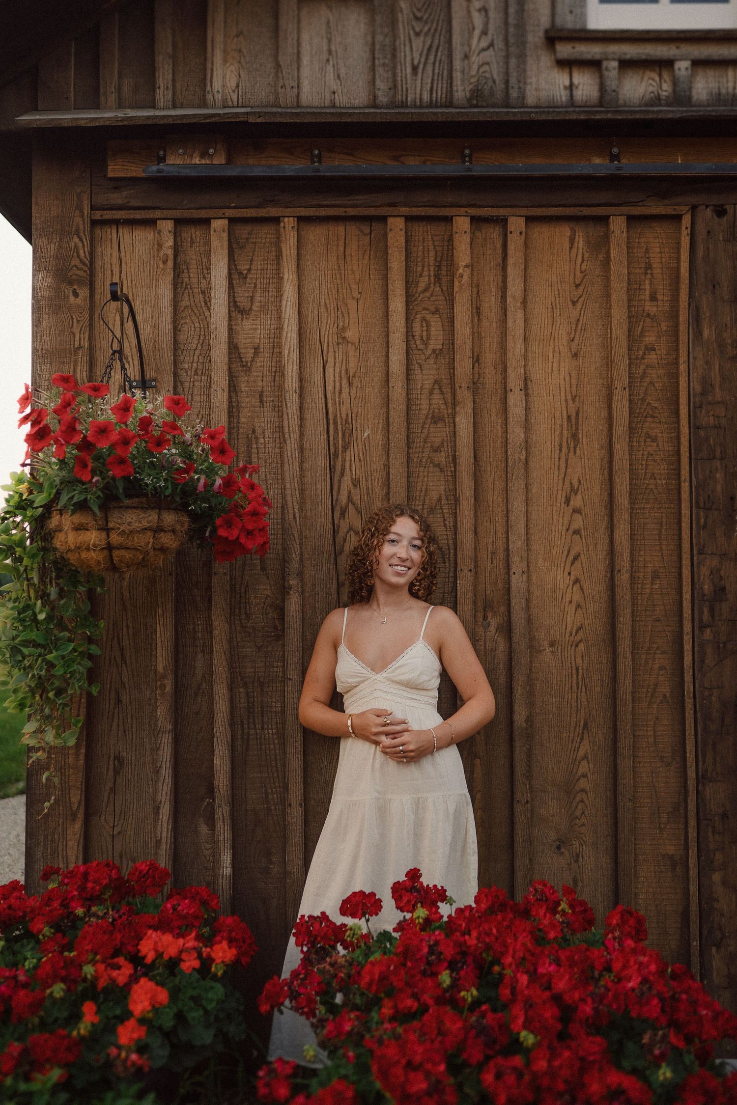 A candid series of poses against a rustic wooden wall surrounded by vibrant red flowers.