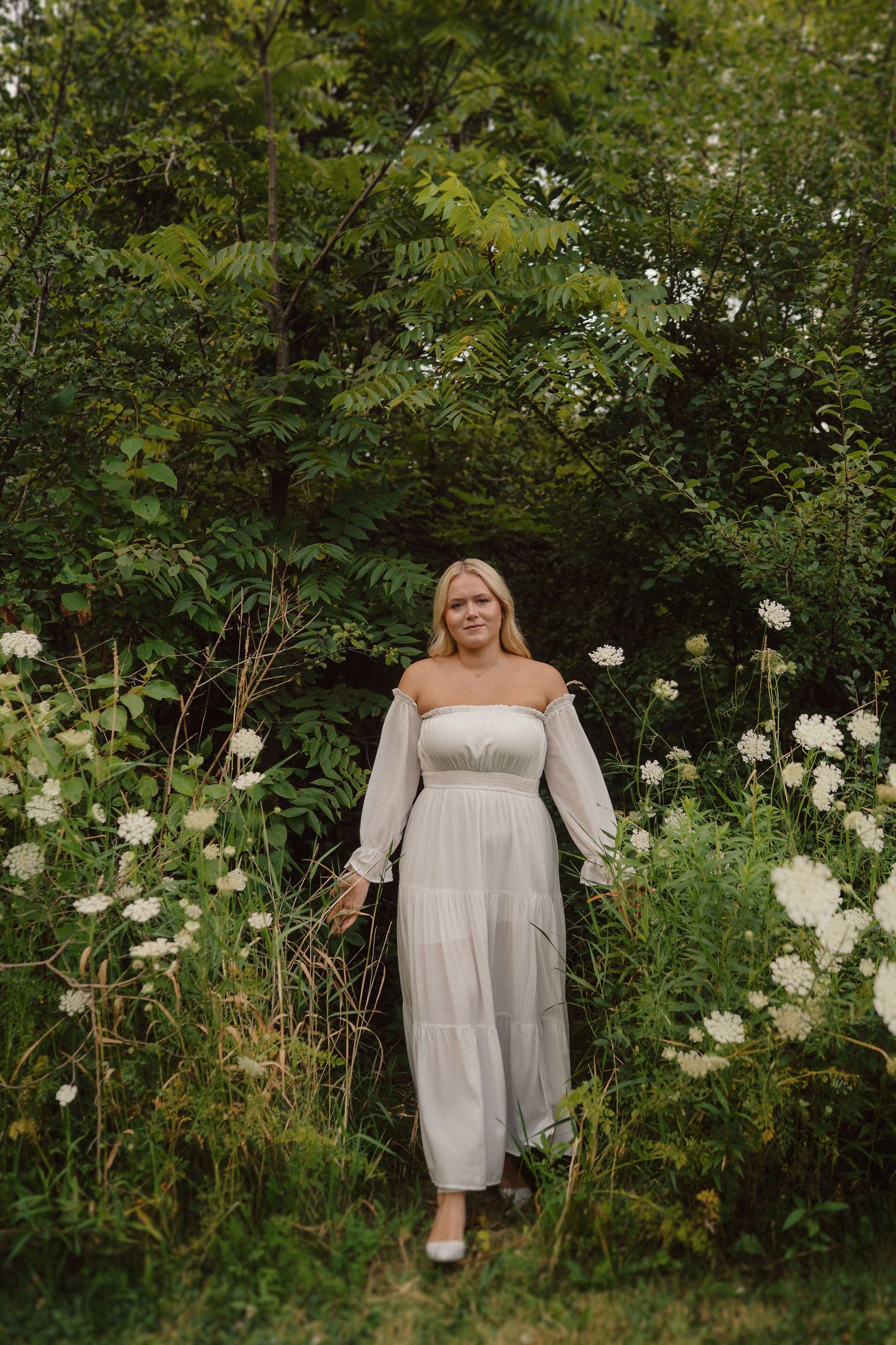 A flowing white dress stands out against lush green foliage and white flowers in a summer garden setting.