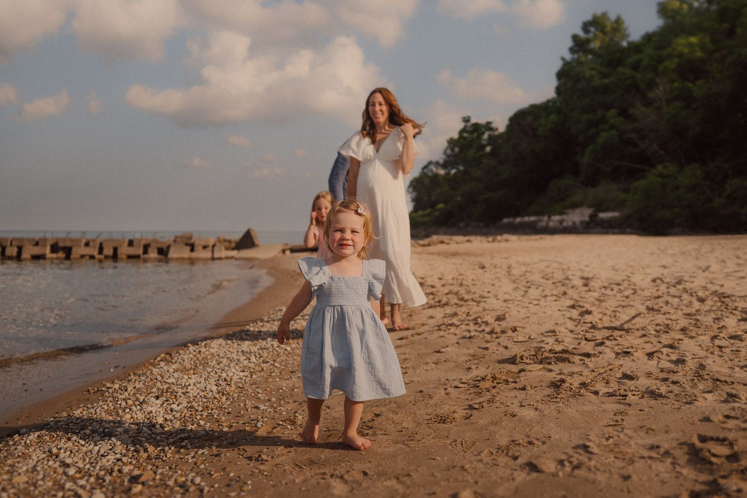 Candid family moment captured during sunset walk along a peaceful beach with jetty in background.