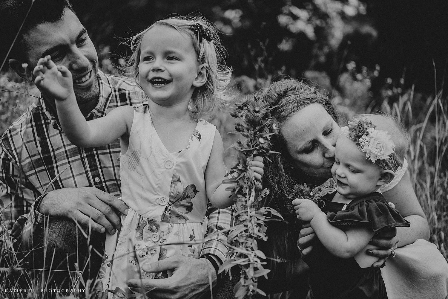 A joyful black and white portrait of a family laughing together in tall grass.