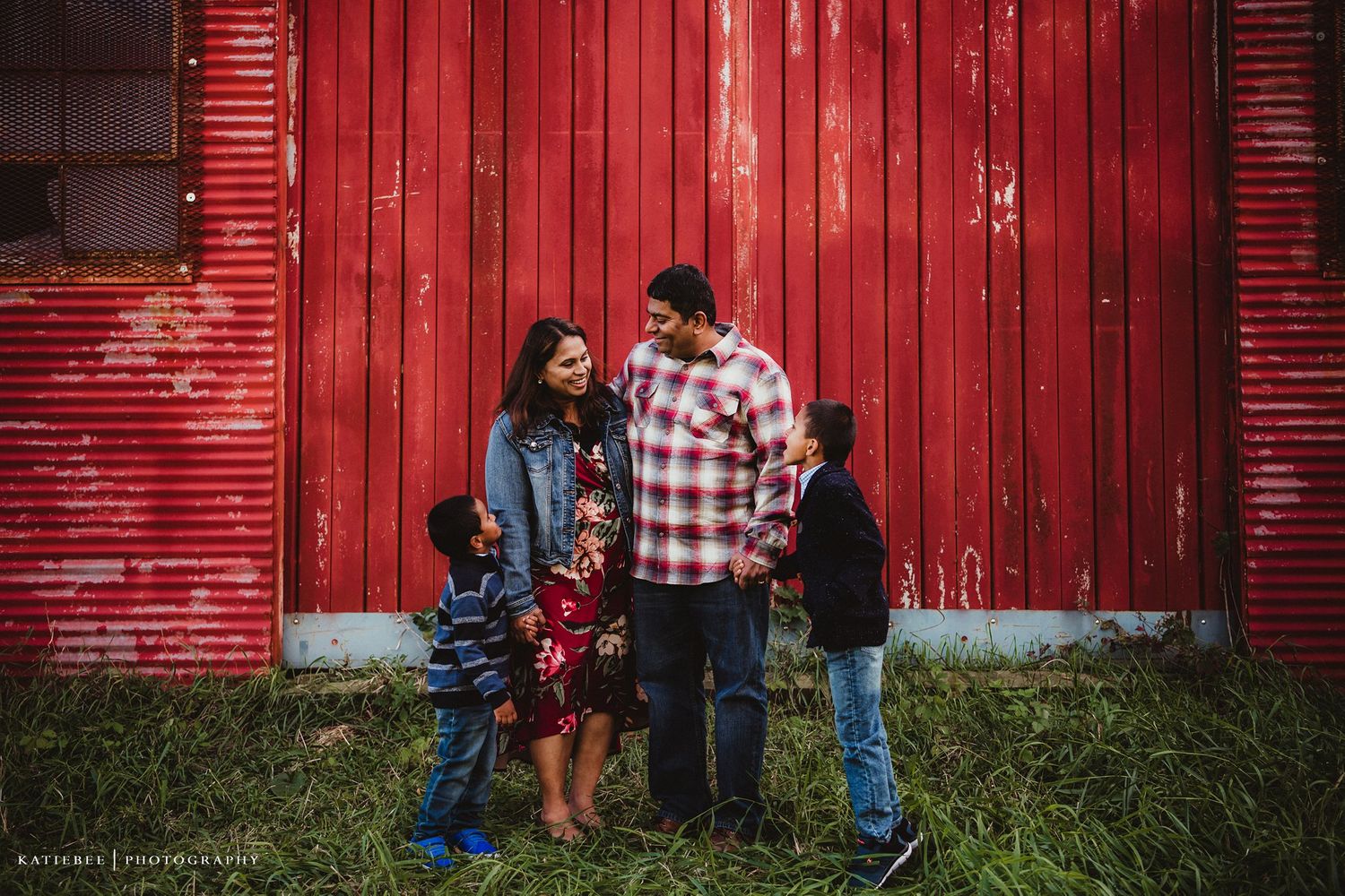 Family portrait against vibrant red barn in rustic outdoor setting.