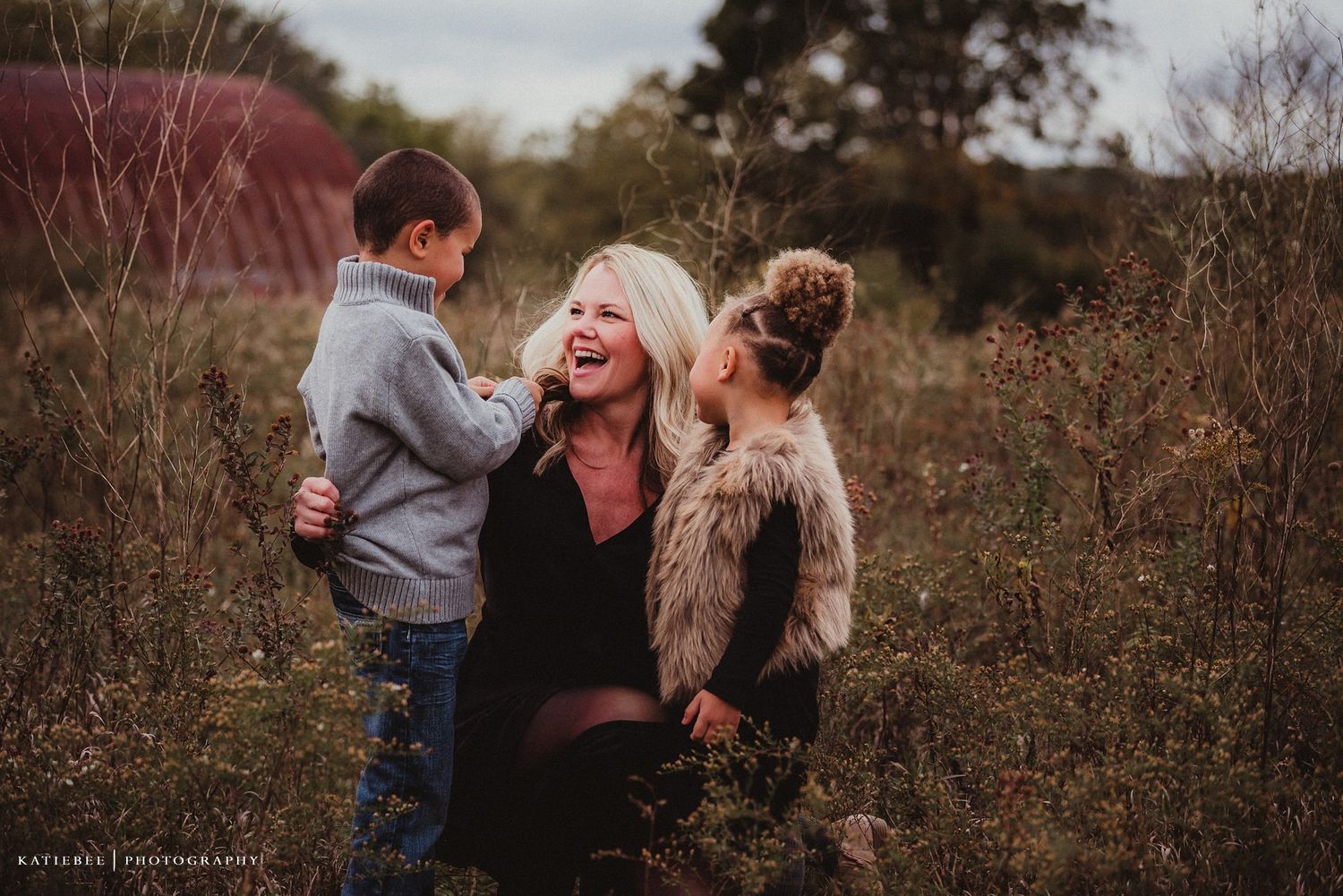 Candid family portrait of people sharing joyful moments together in an autumn field at sunset.