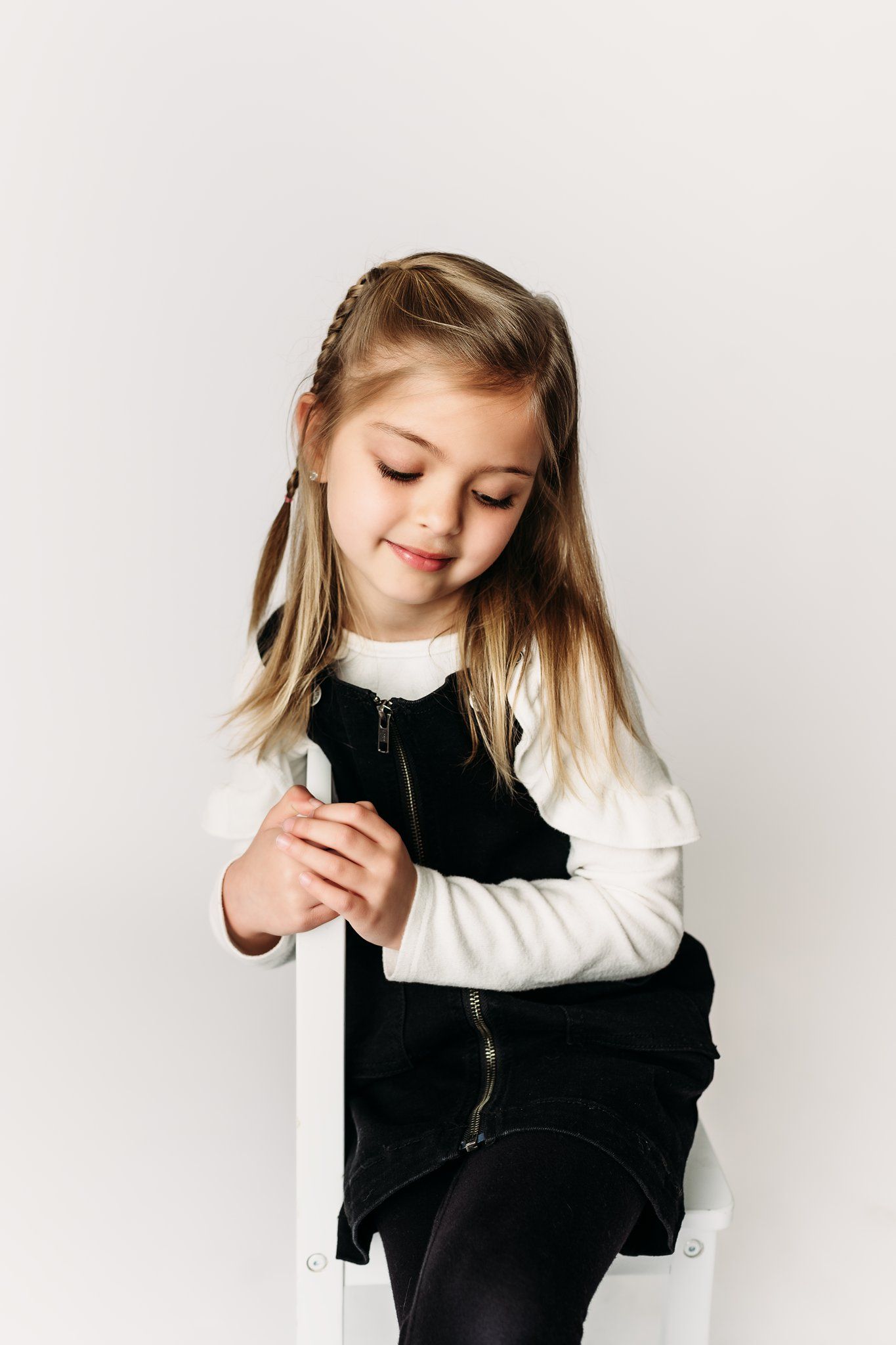 A child in black and white outfit leans against a white surface with eyes closed.