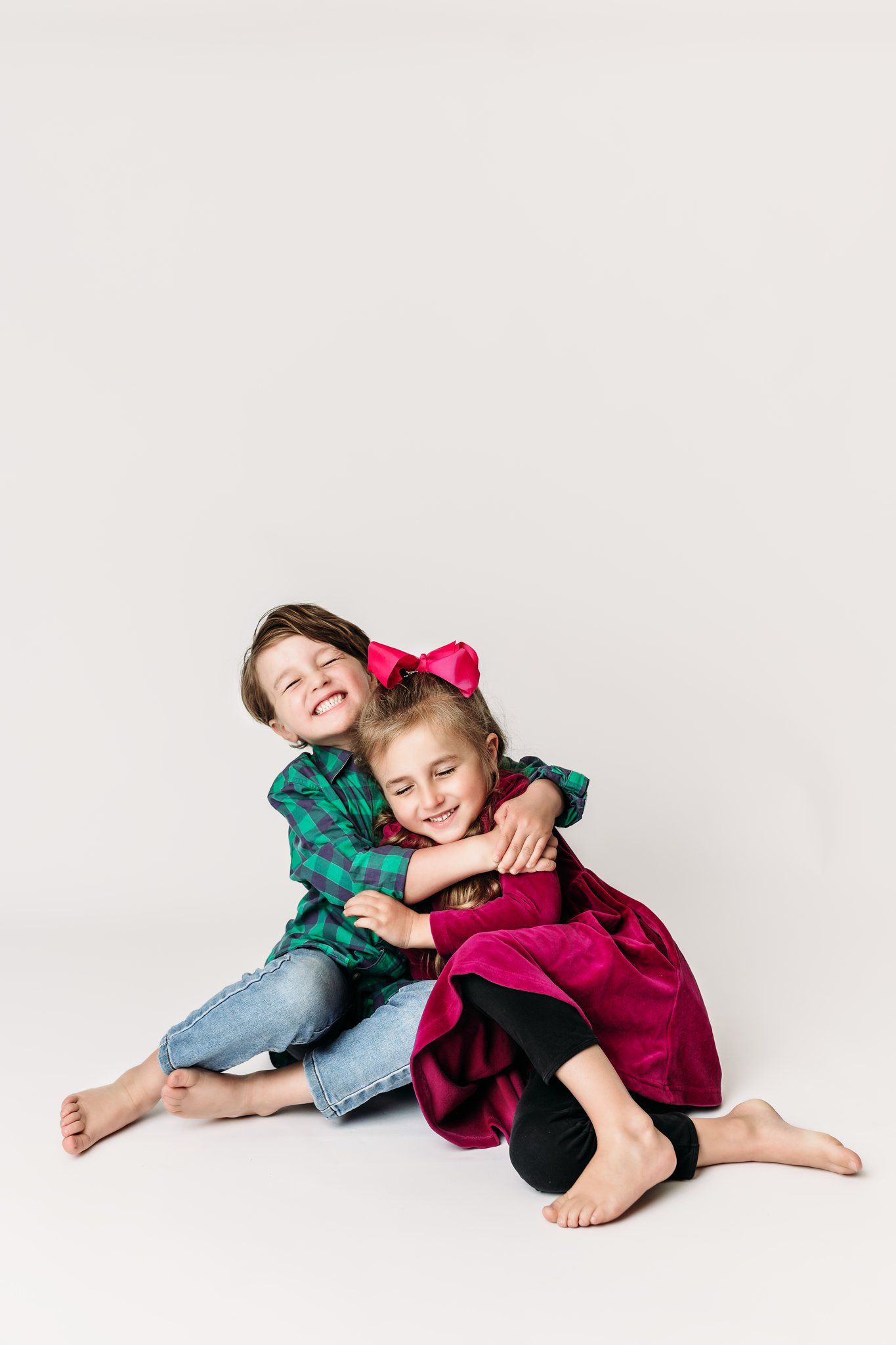 Two children in holiday outfits hugging and smiling on white background.