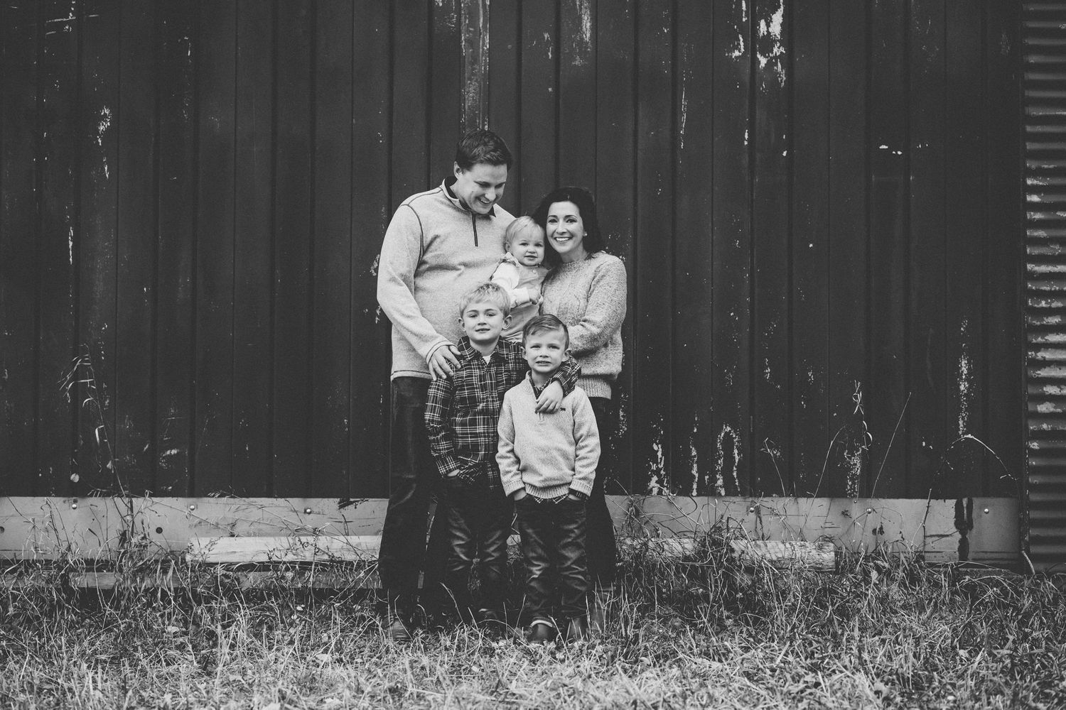 Black and white portrait of a family with three children posed in front of a weathered barn.