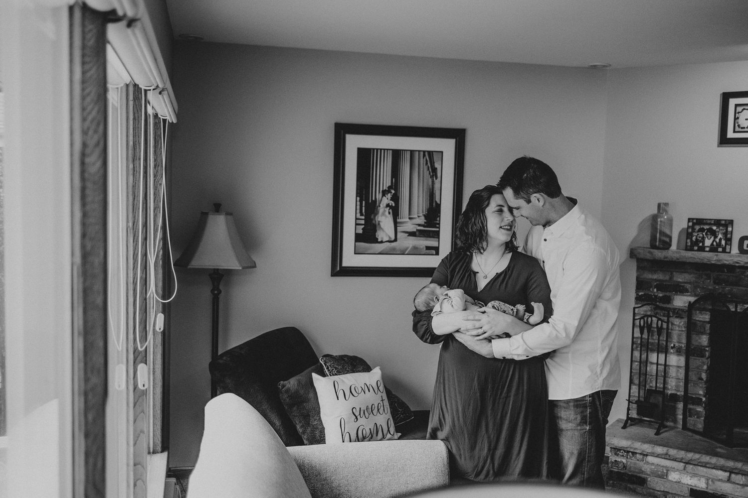 A black and white photograph captures a tender moment with a newborn in a living room setting.