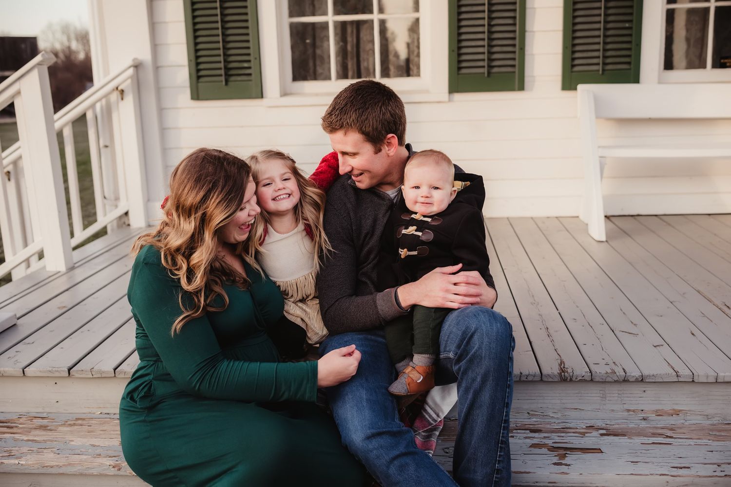 A family sits together on a wooden porch during a casual outdoor photo shoot.