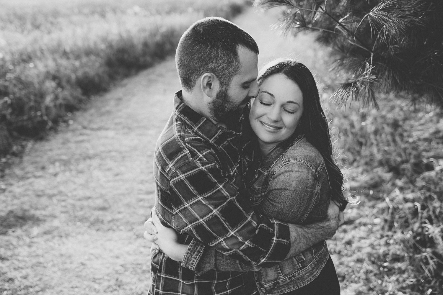 Black and white photo of couple sharing intimate moment on nature path.