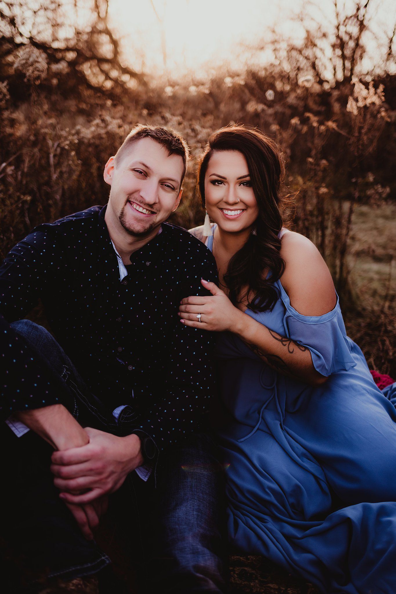 Casual outdoor portrait of happy couple sitting together in rustic field setting.