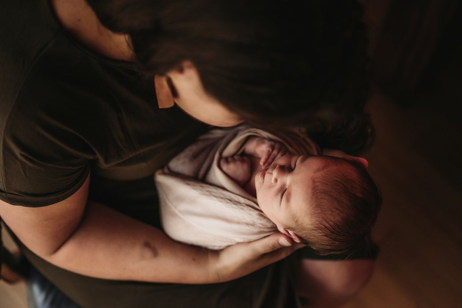 Newborn baby sleeps peacefully while being cradled in soft lighting.