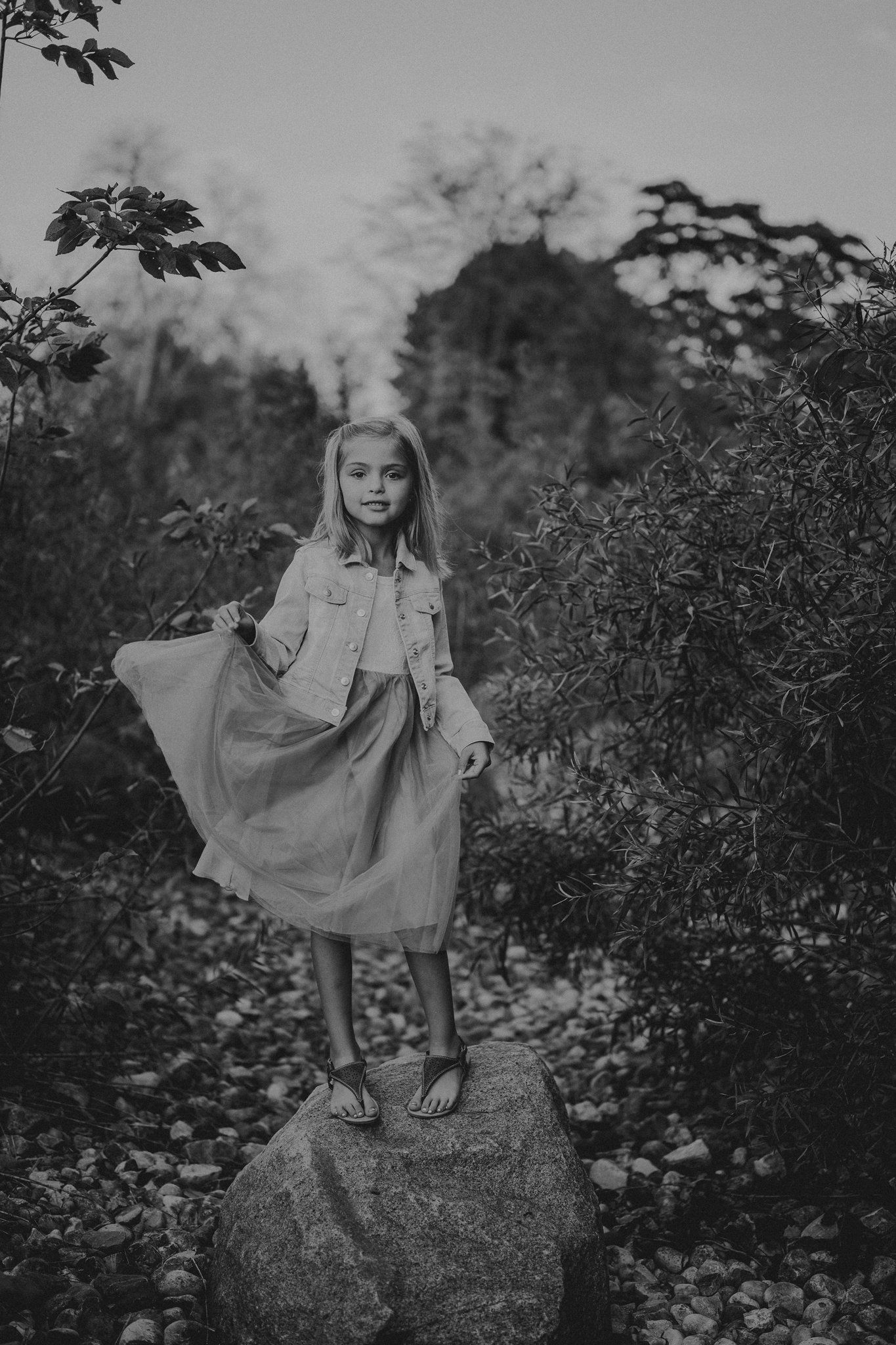 A black and white portrait of someone standing on a rock surrounded by foliage.