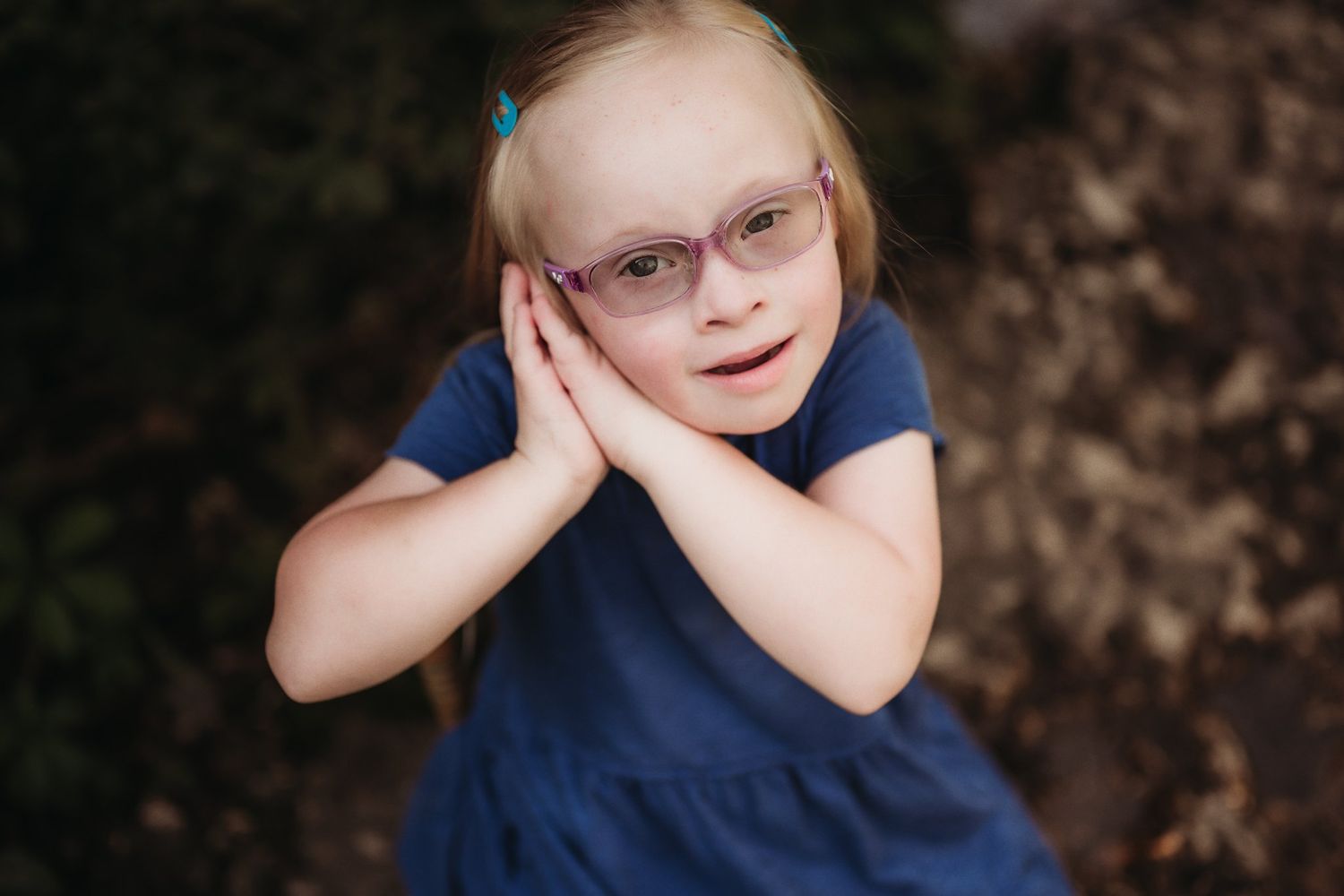 Young person in navy blue dress making playful expression while resting head in hands.