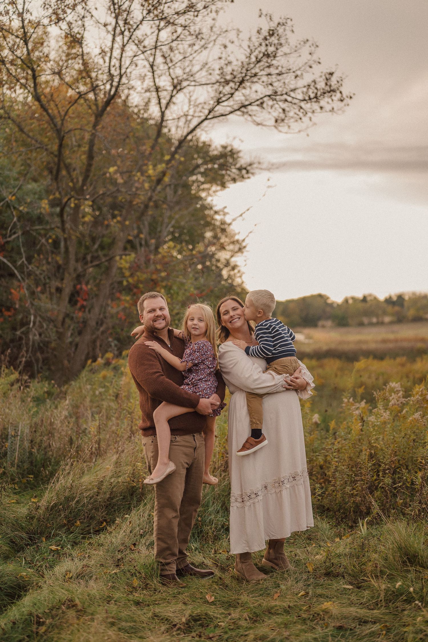 A happy family embraces and laughs together in a scenic autumn field at golden hour.