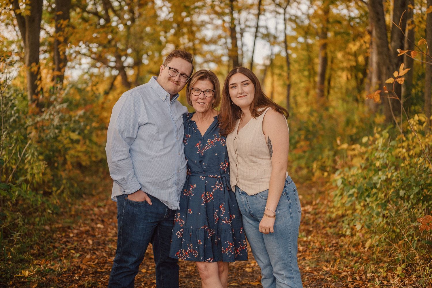 A group poses together in a wooded area during autumn with golden sunlight filtering through the trees.