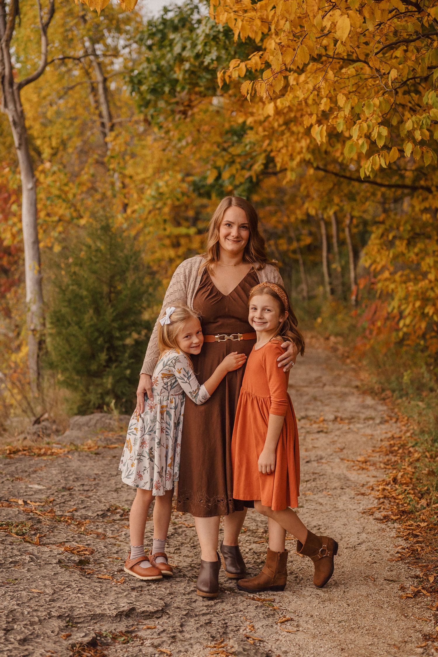 Three people in coordinated brown and orange outfits pose on autumn trail with golden leaves.