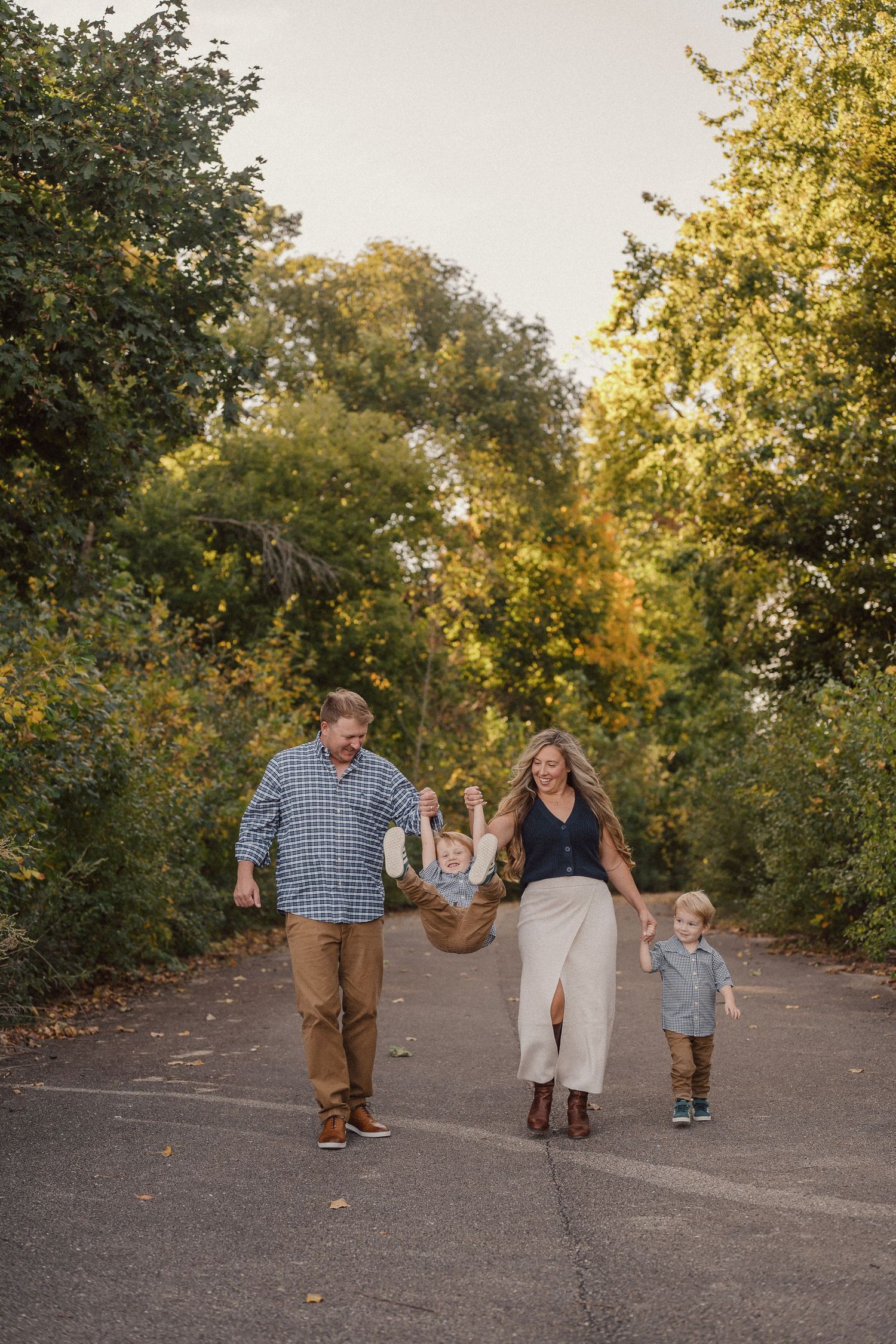 Family walking together on a tree-lined path during golden hour in autumn.