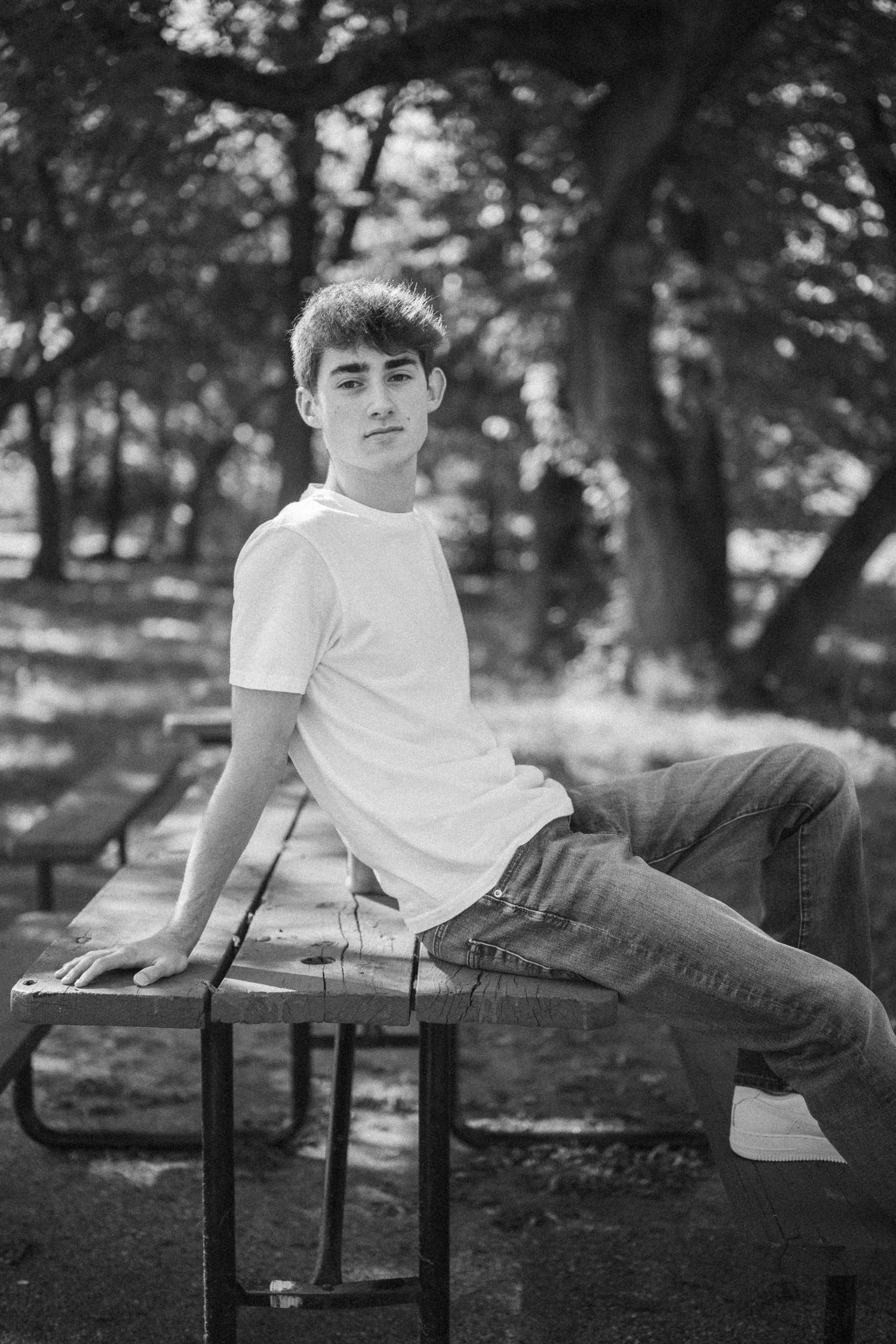 Black and white photo of someone lounging casually on a wooden bench in a park setting.