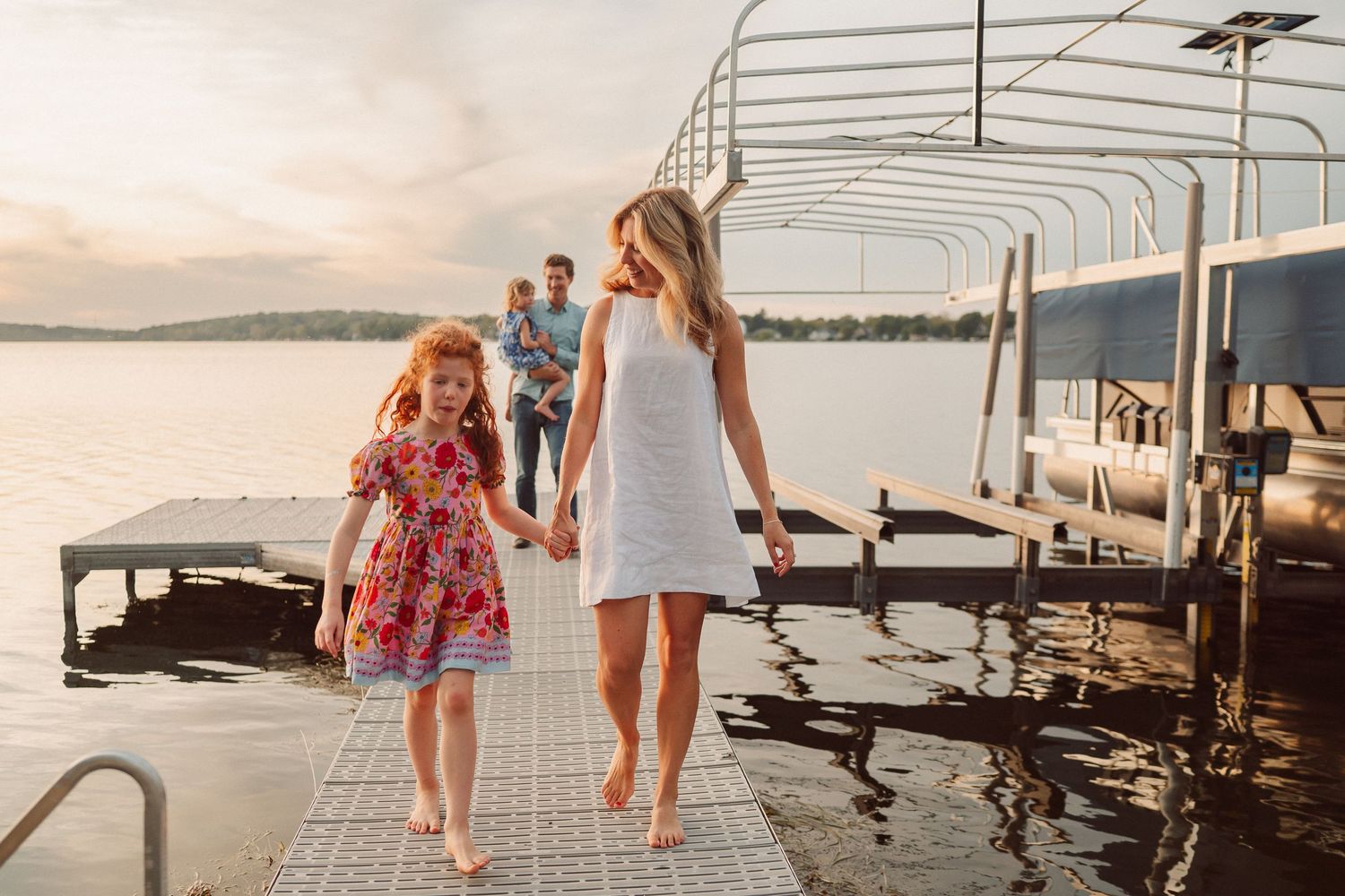 People enjoying a summer evening on a wooden dock by the lake at sunset with boats in the background.