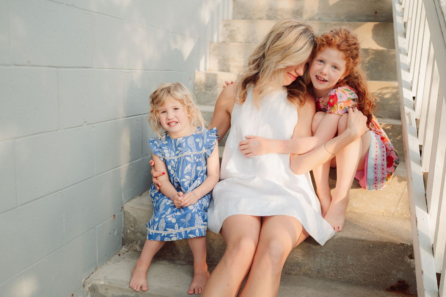 Children sit on white stairs in summer outfits during a bright sunny day.