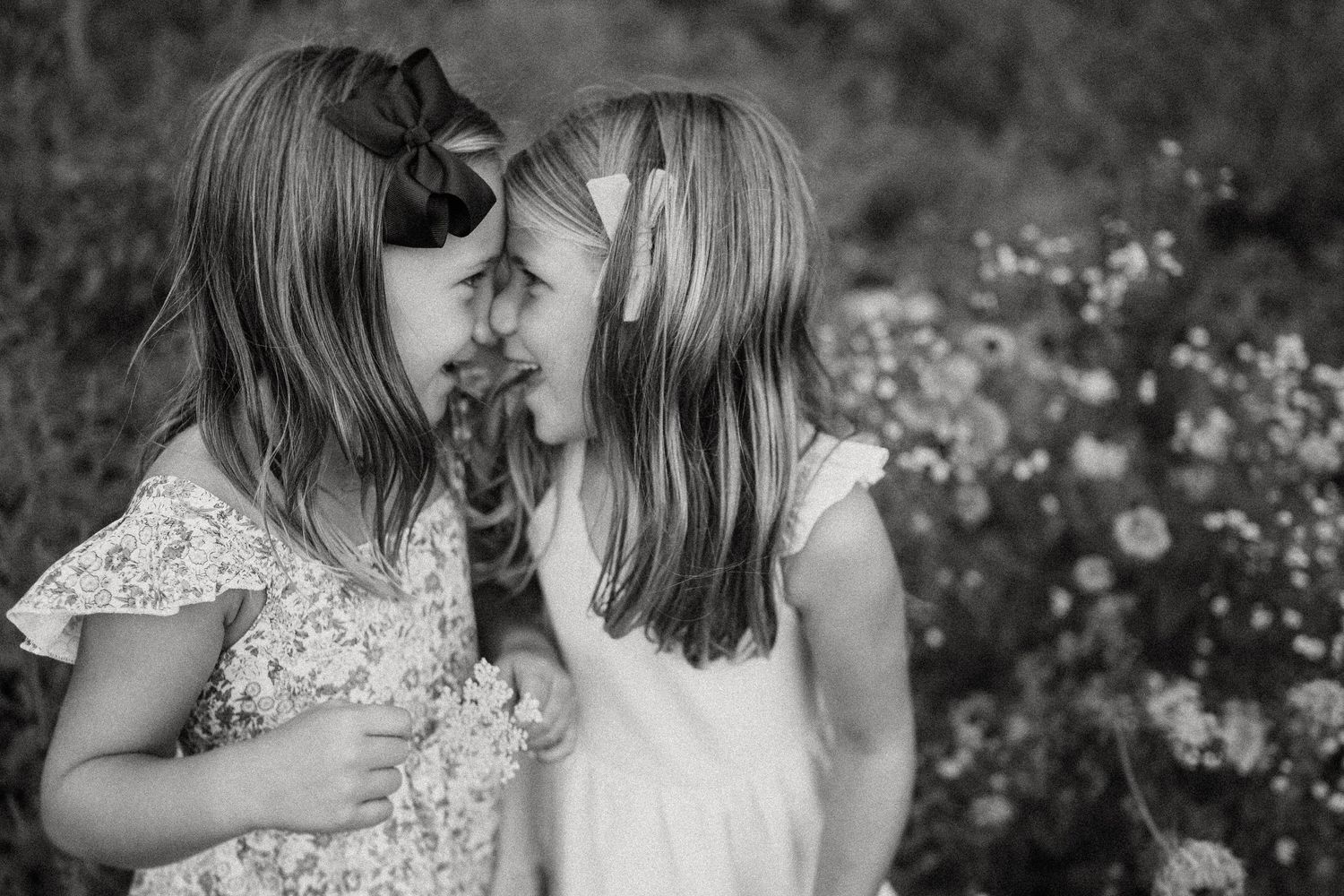 Black and white portrait of two children sharing a sweet moment among blooming flowers.