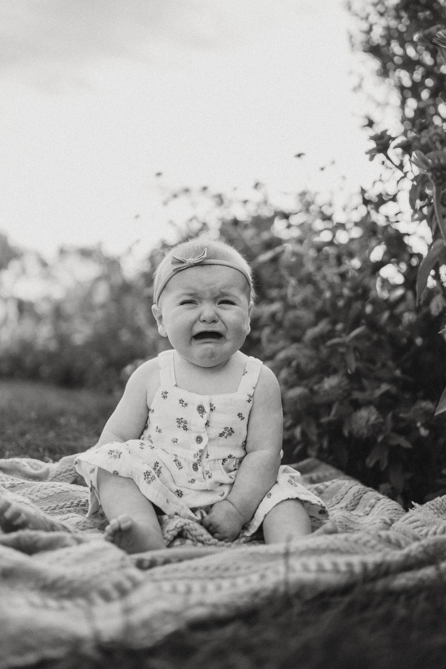 Black and white capture of joyful baby laughing while sitting on blanket outdoors.