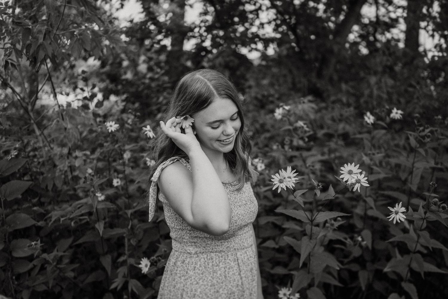Black and white portrait of someone in a patterned dress standing among wildflowers.