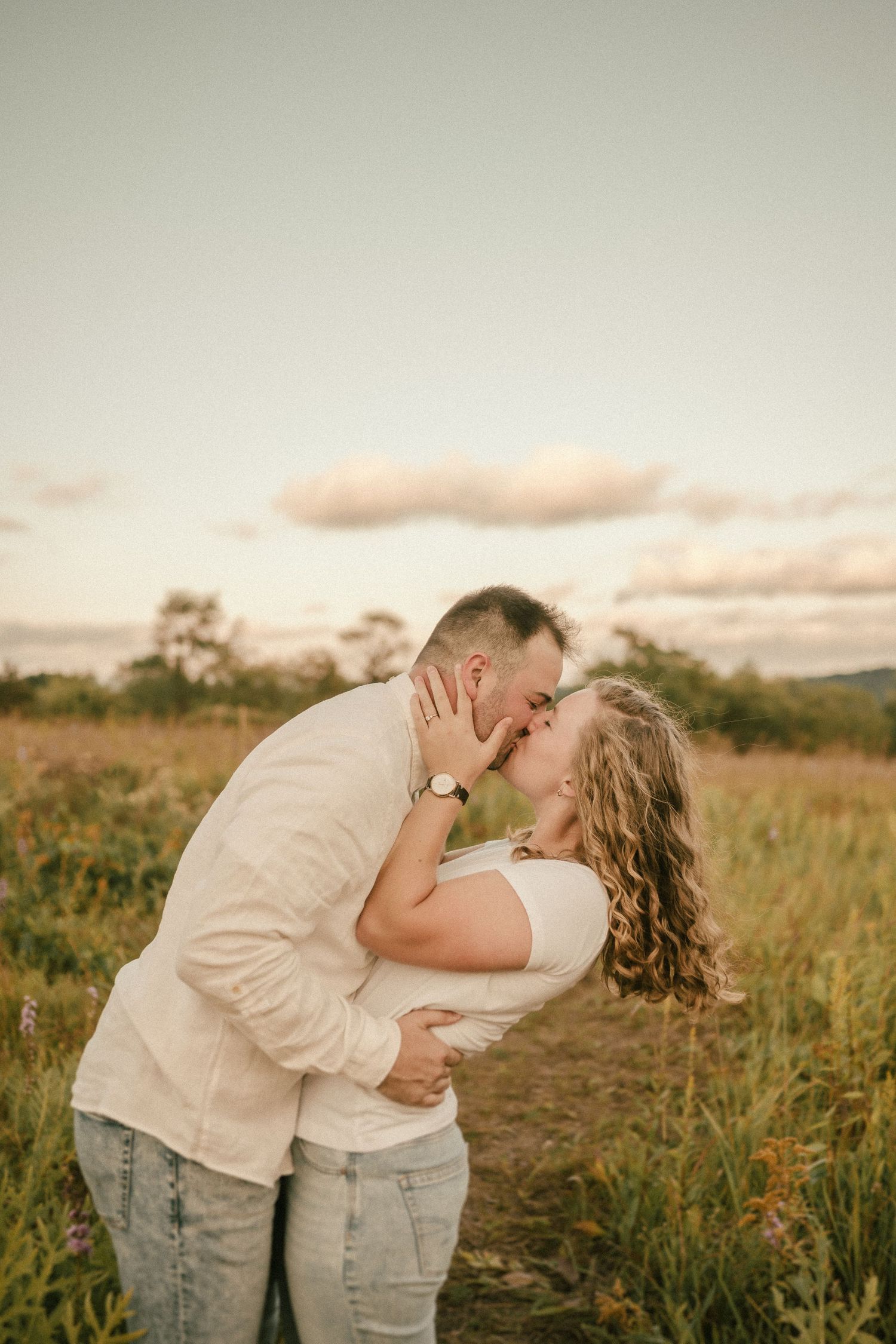 A tender moment between a couple kissing in a sunlit meadow at dusk.