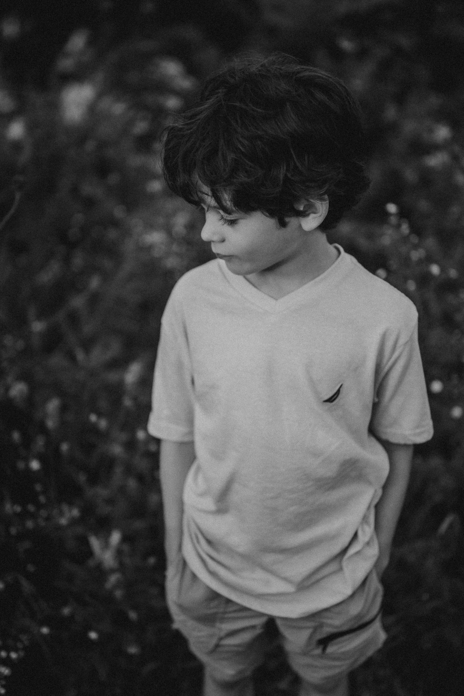 Black and white portrait of a child in casual clothing standing in a garden.