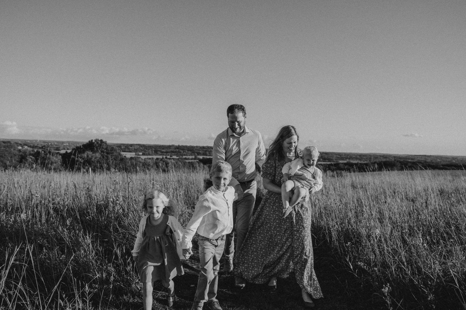 Black and white candid family photo taken in a grassy field with mountains in the distance.