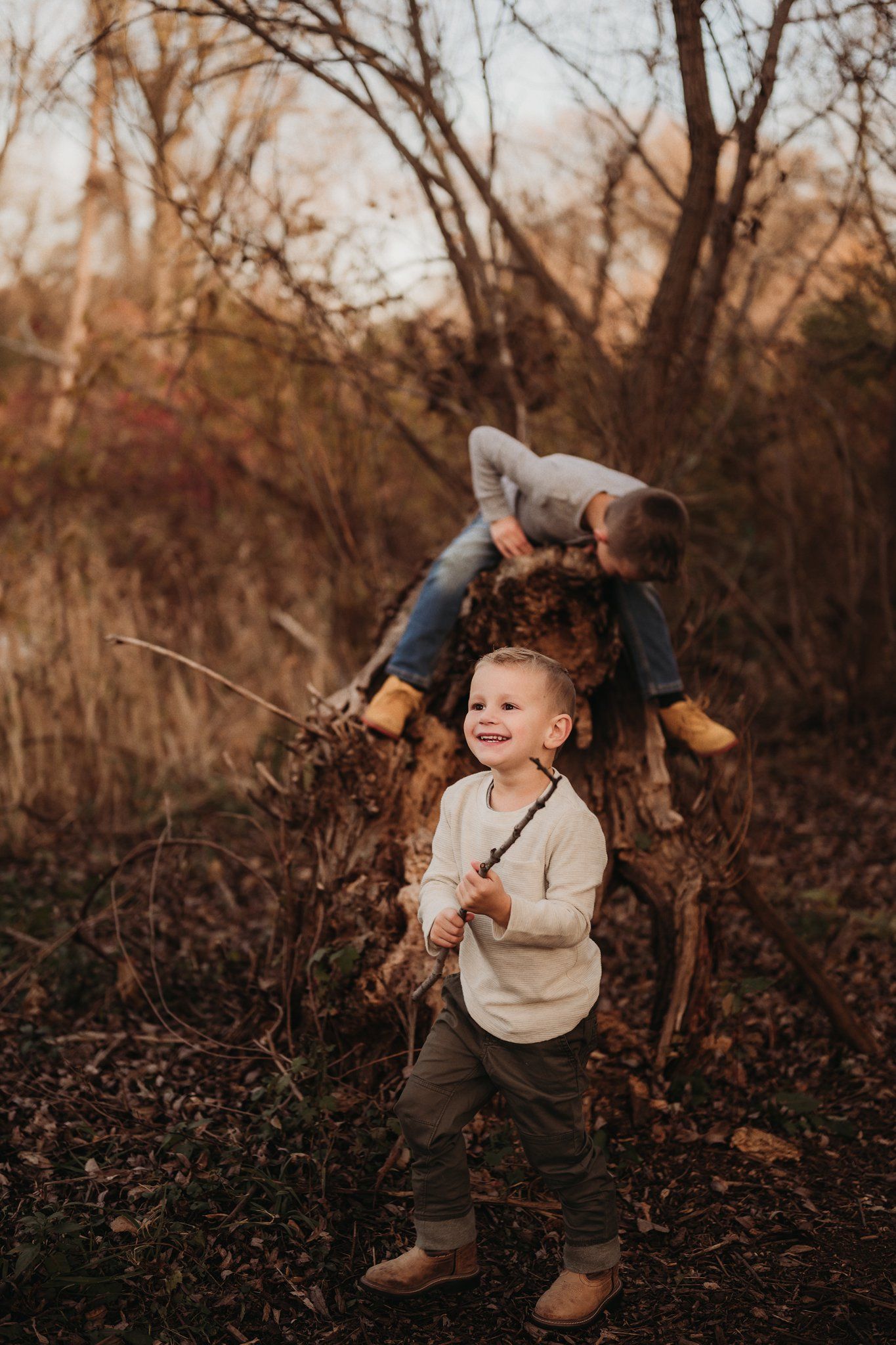 A child holding a stick explores autumn woods while playing outdoors at sunset.