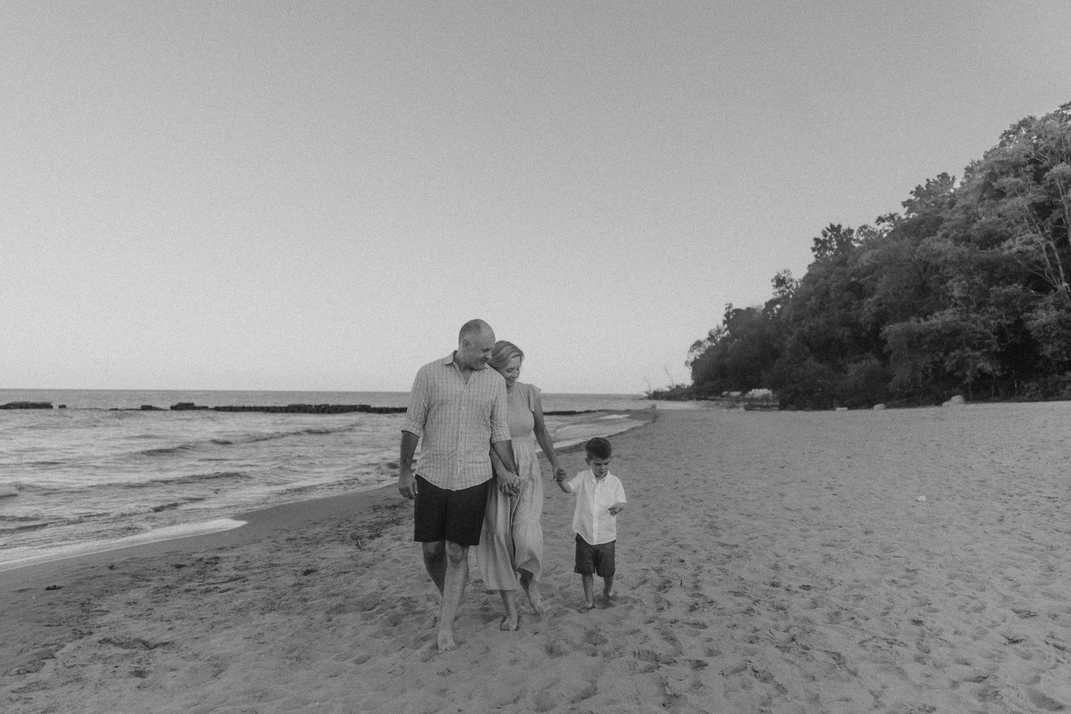 Three figures walking along a sandy beach with tree-covered cliffs in the background.