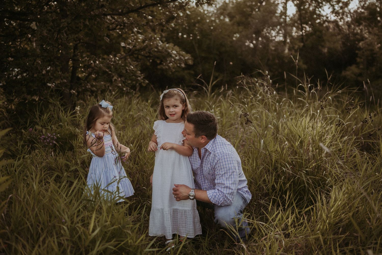 Intimate family moment captured in evening light among tall grass.